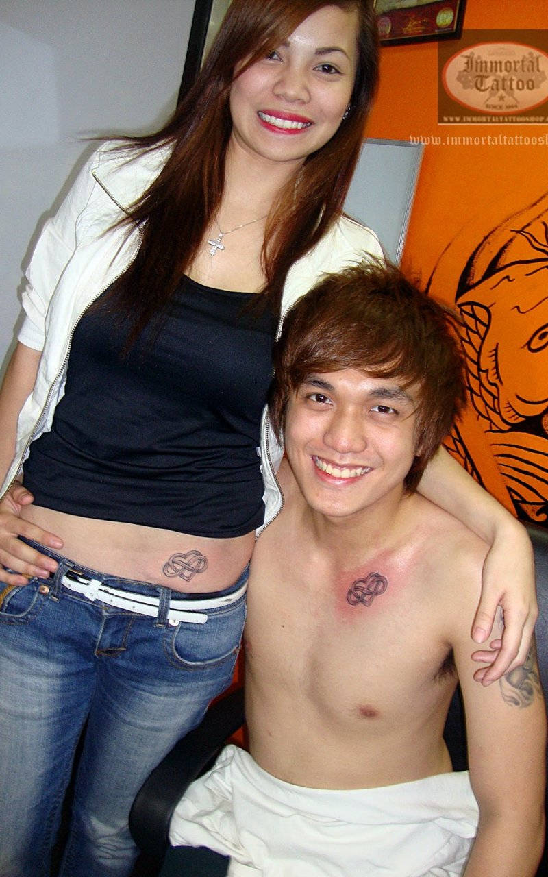 cute couple matching 桌布 壁紙 — 一對微笑的年輕情侶，臀部與胸口有相配的無限刺青，在刺青店一起擺姿勢。
