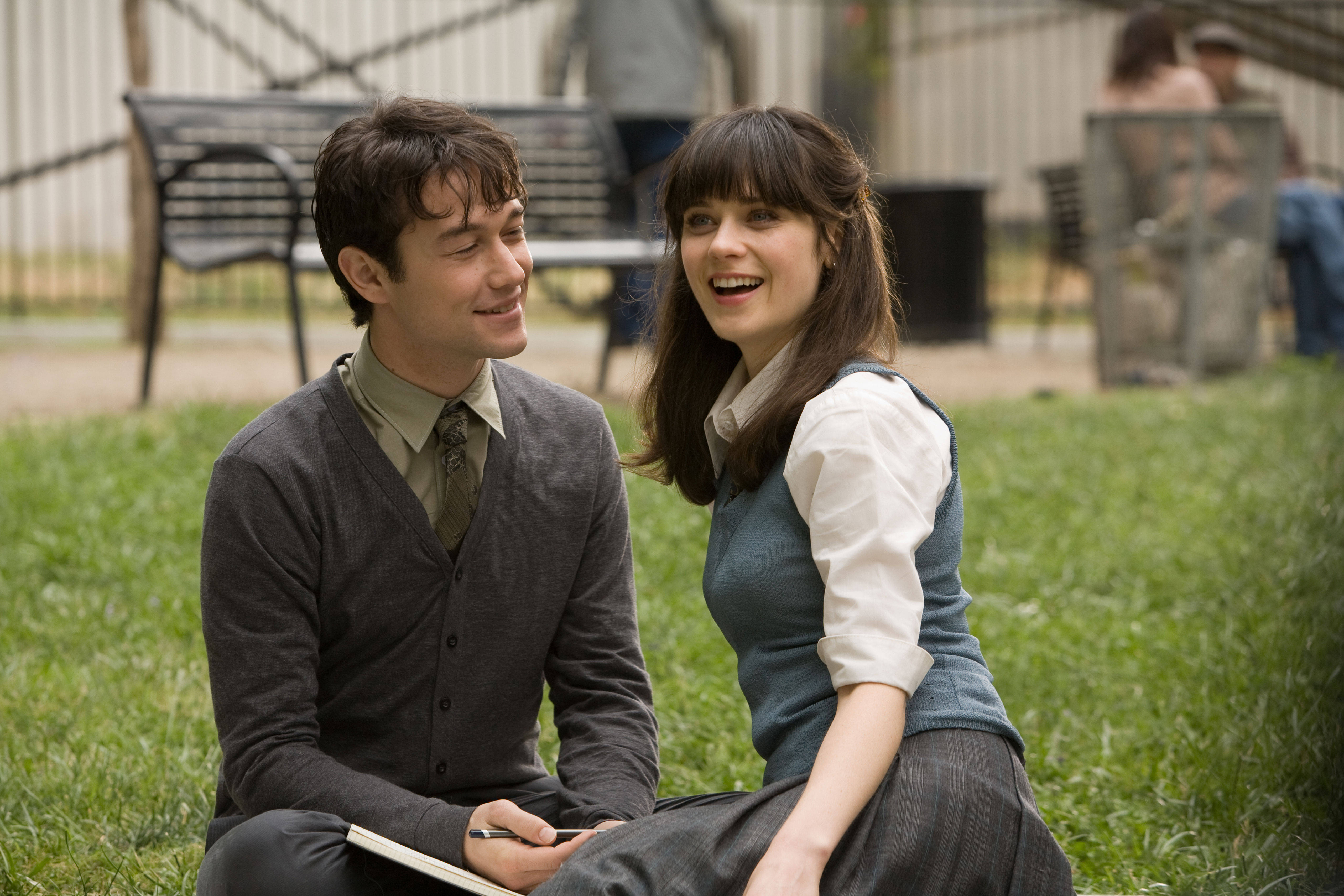 500 Days Of Summer 桌布 壁紙 — 一對微笑的年輕情侶坐在草地上，在公園環境中分享歡樂的戶外時光。