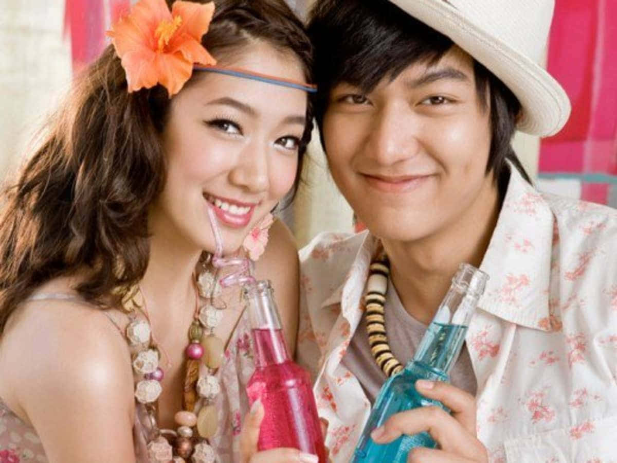 Beautiful Couple 桌布 壁紙 — 一對微笑的年輕情侶穿著熱帶服飾，戴著花環頭帶和吸管，啜飲色彩繽紛的飲料。