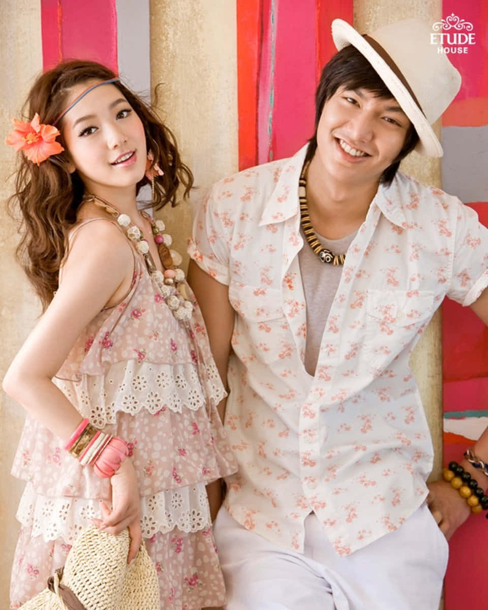 Beautiful Couple 桌布 壁紙 — 一對微笑的年輕情侶穿著花卉圖案服裝，在色彩繽紛的條紋牆前擺姿勢，色調溫暖。