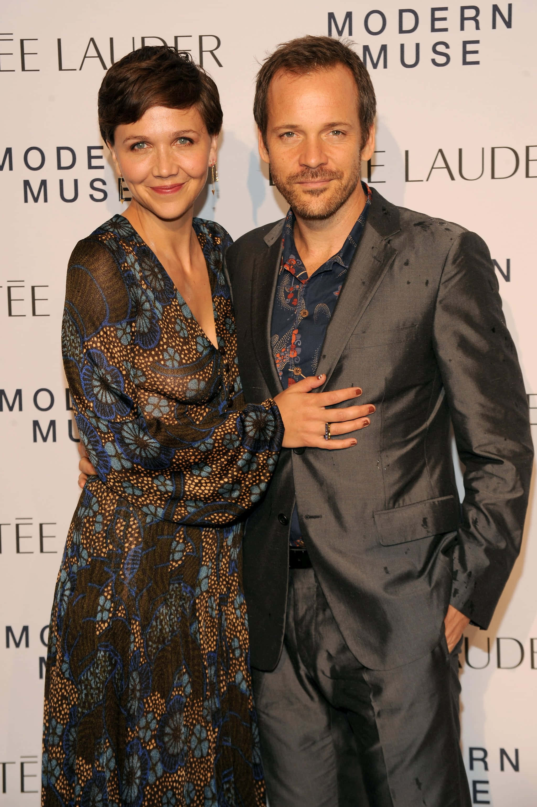 Peter Sarsgaard 桌布 壁紙 — 一對微笑的情侶在品牌背景前，穿著優雅服裝，在溫暖燈光下於正式活動中一起擺姿勢。