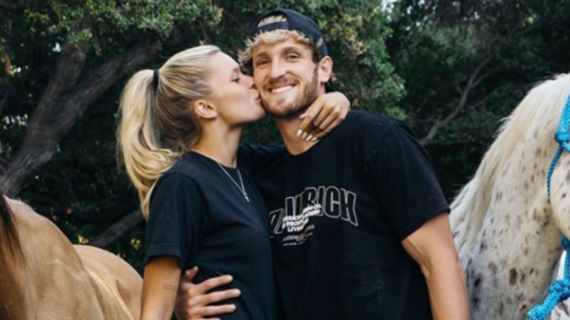 Logan Paul 桌布 壁紙 — 一對微笑的情侶在戶外，在枝葉茂密的樹下，與兩匹馬旁邊分享溫柔的親吻。