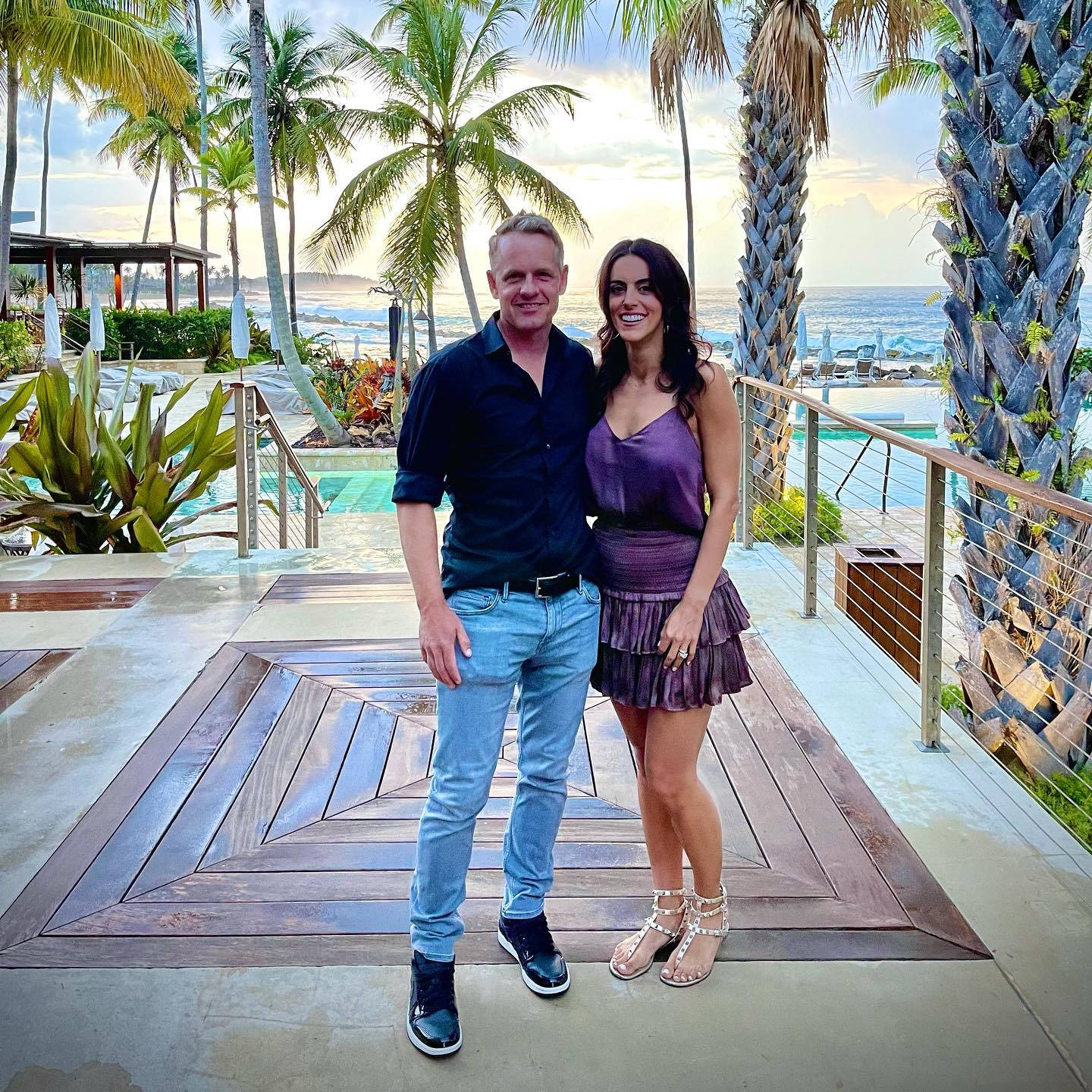 Wife 桌布 壁紙 — 一對微笑的情侶在日落時分，在棕櫚樹和海洋景觀的泳池旁木甲板上擺姿勢。