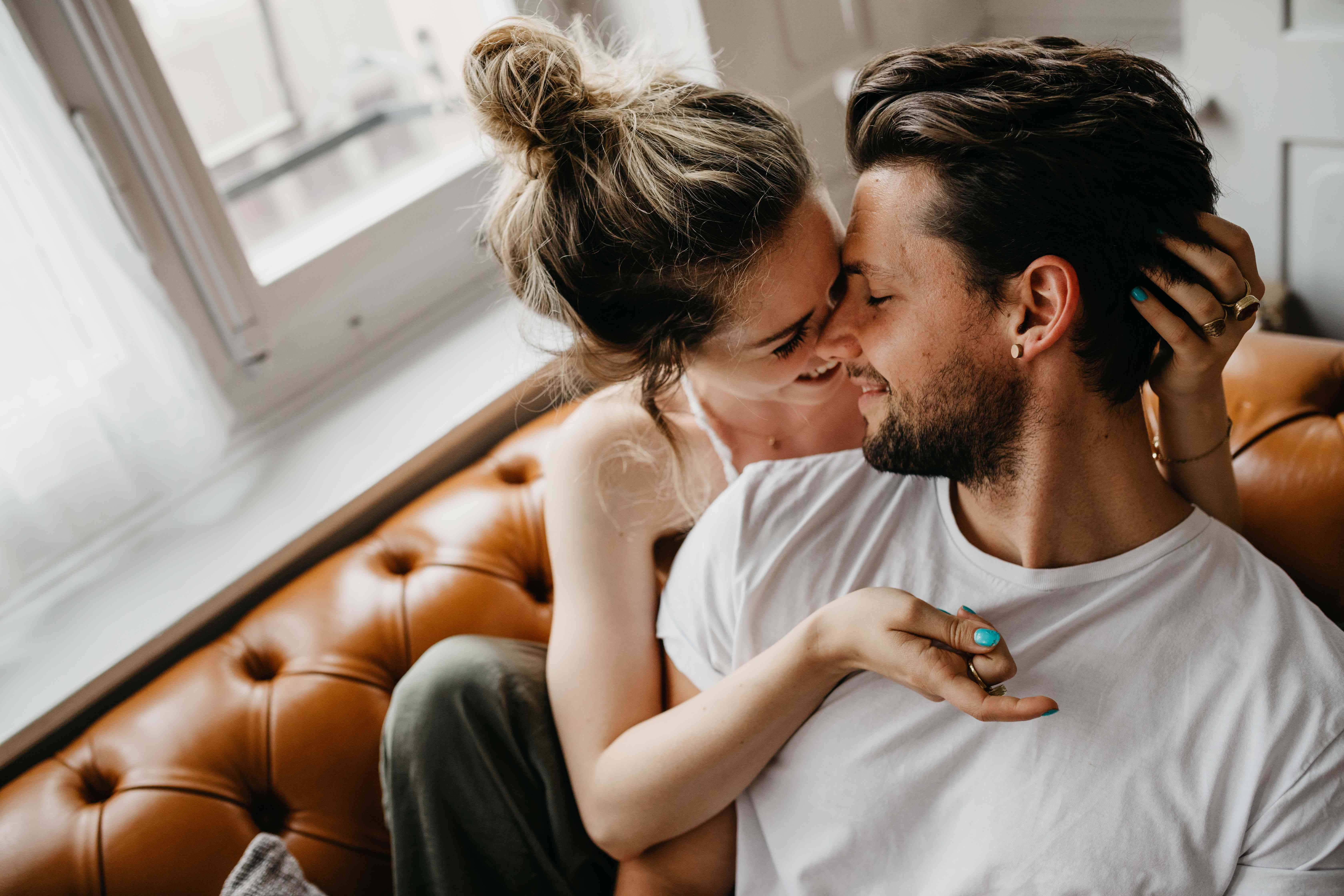 Romantic Love 桌布 壁紙 — 一對微笑的情侶在明亮的窗邊棕色皮革沙發上分享親密時刻。