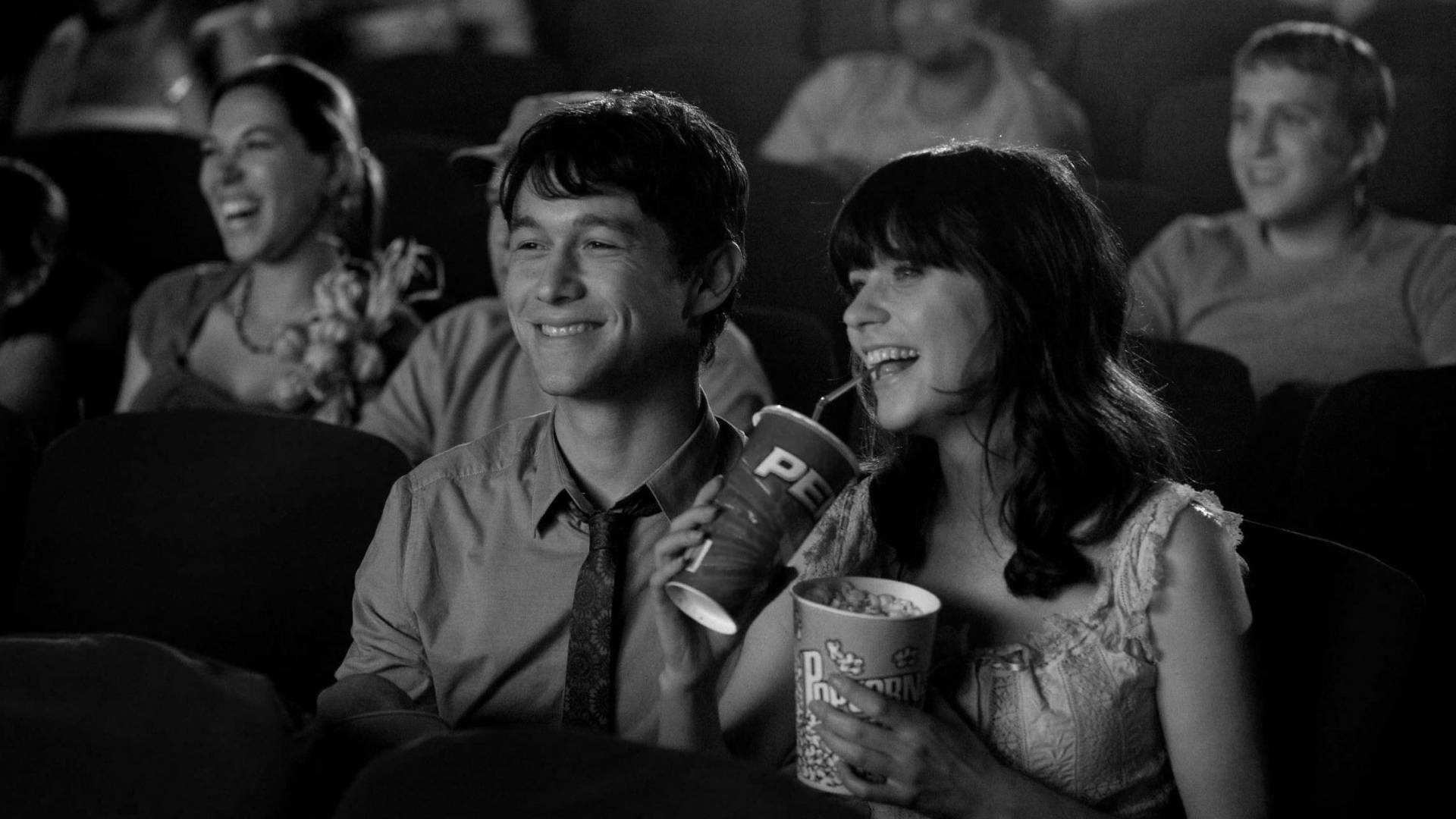 500 Days Of Summer 桌布 壁紙 — 一對微笑的情侶在昏暗的電影院裡一起大笑，手裡拿著爆米花，周圍有其他觀眾。