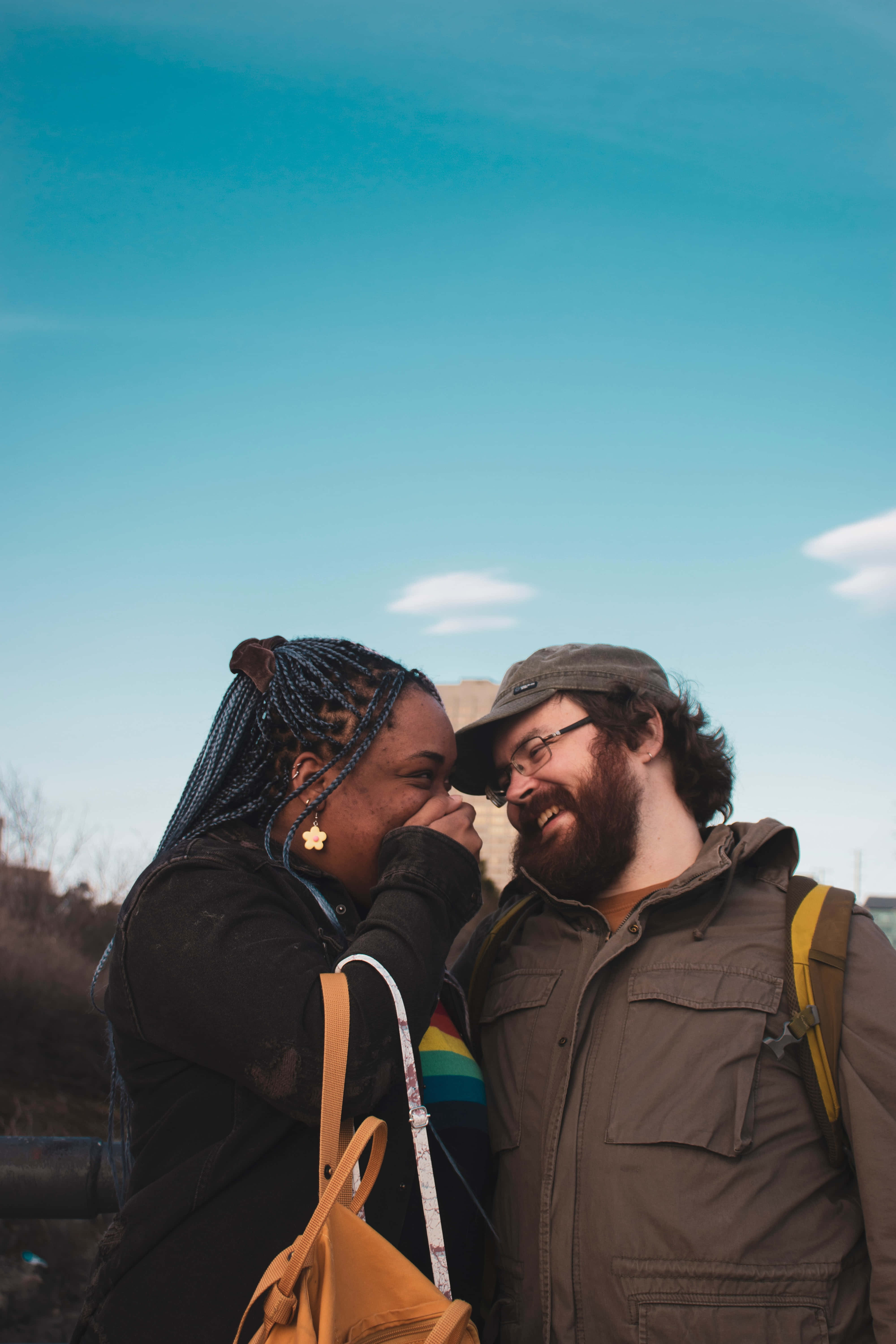 Interracial 桌布 壁紙 — 一對微笑的情侶在晴朗藍天和柔軟白雲下分享溫馨時刻。