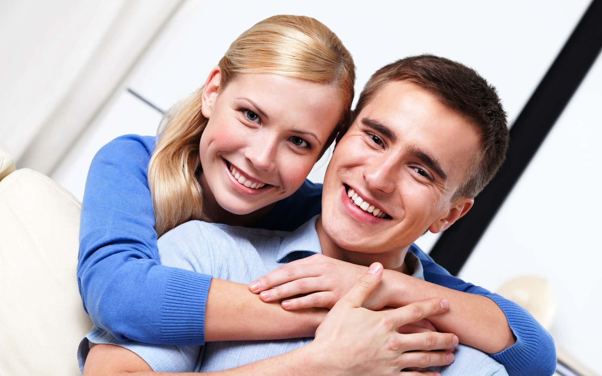 Wife 桌布 壁紙 — 一對微笑的情侶在柔和的燈光和現代幾何背景的沙發上溫暖地擁抱。