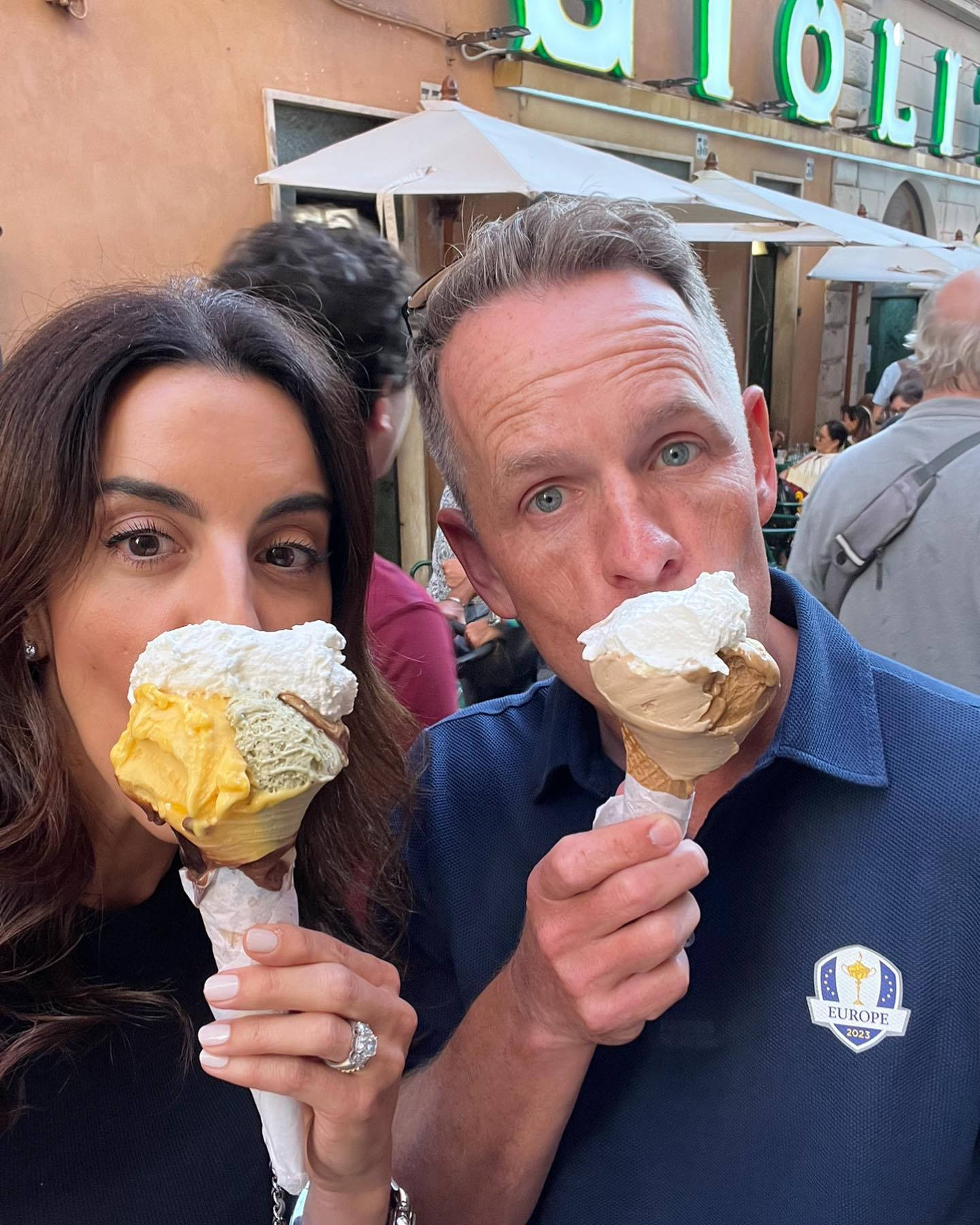 Ice Cream 桌布 壁紙 — 一對微笑的情侶在歐洲戶外咖啡館享用冰淇淋甜筒，背景有白色遮陽傘和綠色招牌。