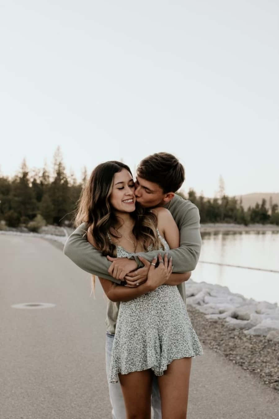 boyfriend 桌布 壁紙 — 一對微笑的情侶在湖邊小徑上擁抱，男人在柔和的金色光線下親吻她的臉頰。