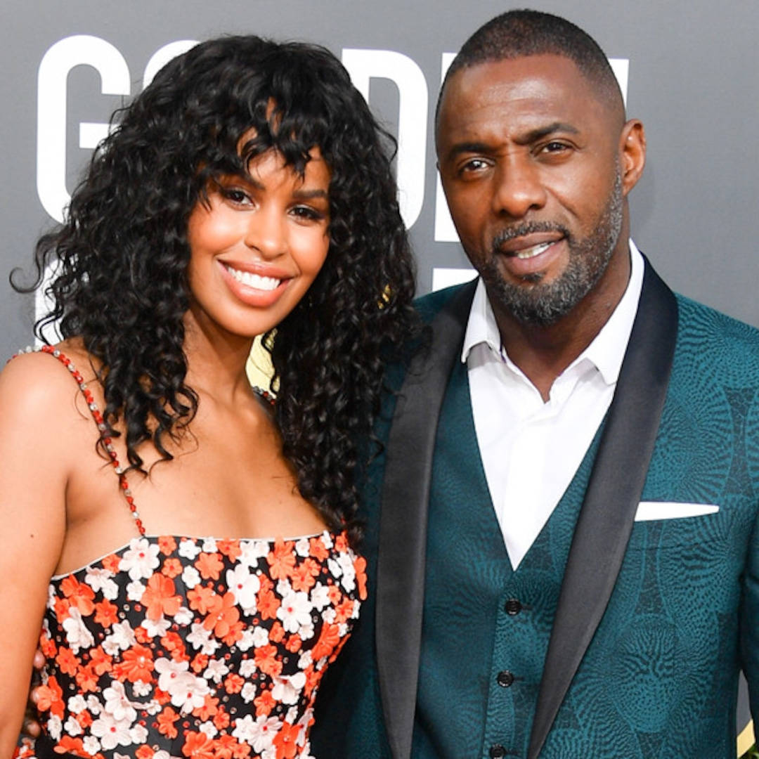 idris elba 桌布 壁紙 — 一對微笑的情侶在灰色背景下，穿著大膽的花卉和青綠色圖案服裝，在華麗的活動中一起擺姿勢。