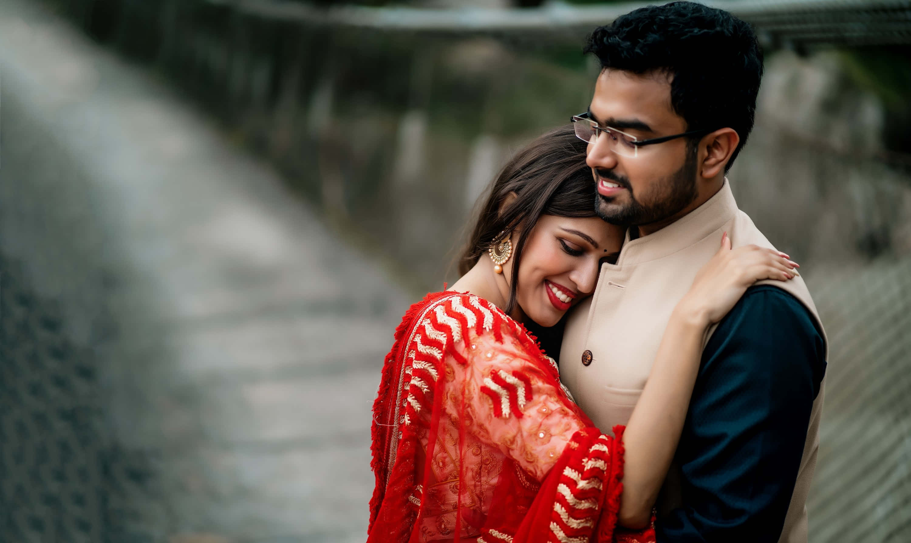 Beautiful Couple 桌布 壁紙 — 一對微笑的情侶在石橋上溫暖擁抱，背景柔和模糊。