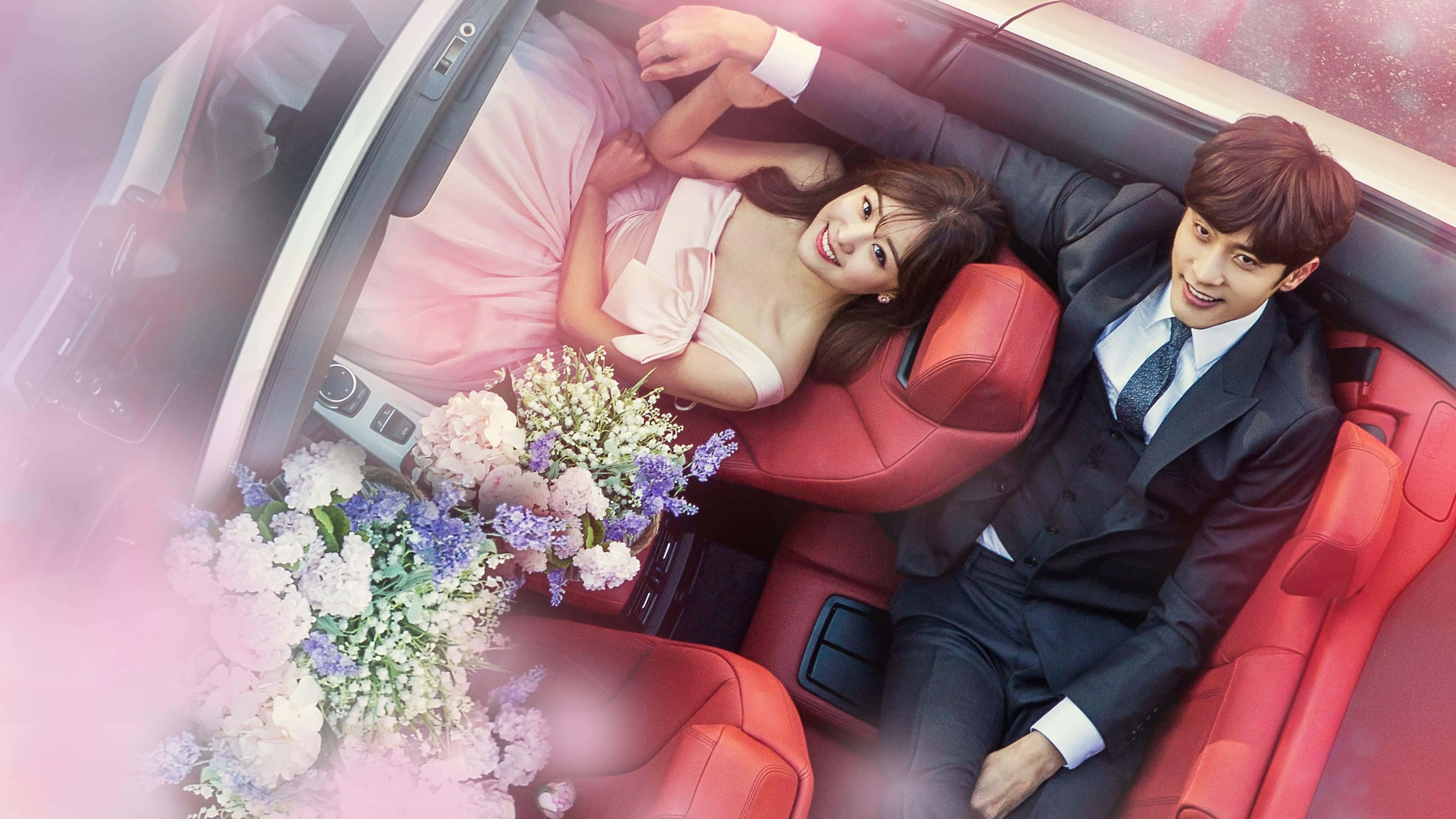 couple love 桌布 壁紙 — 一對微笑的情侶在紅色敞篷車中放鬆，手持繡球花花束，沐浴在柔和的粉紅光中。