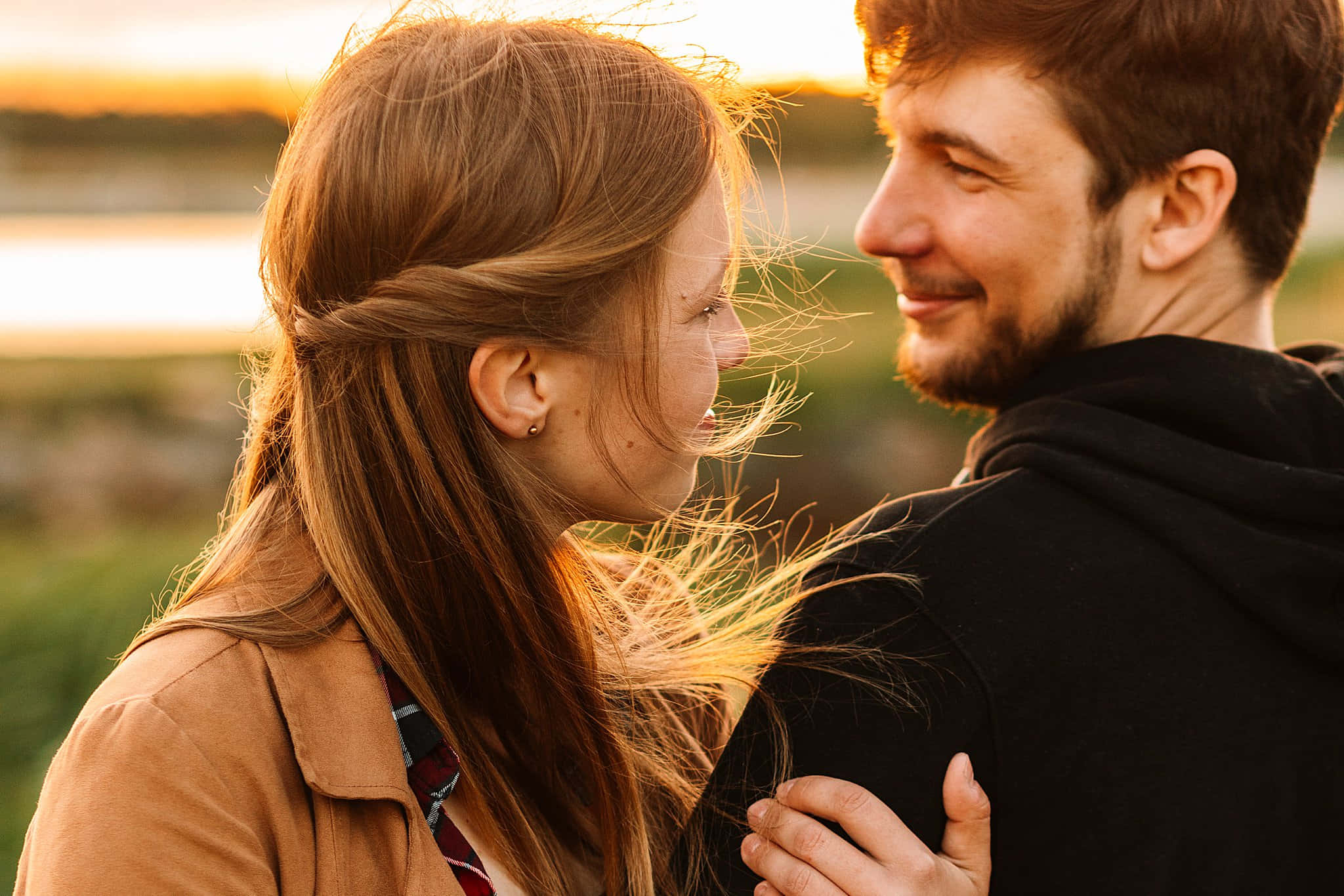 Couple Photography 桌布 壁紙 — 一對微笑的情侶在金色夕陽下，頭髮被光線捕捉，背景模糊的自然環境中分享親密時刻。