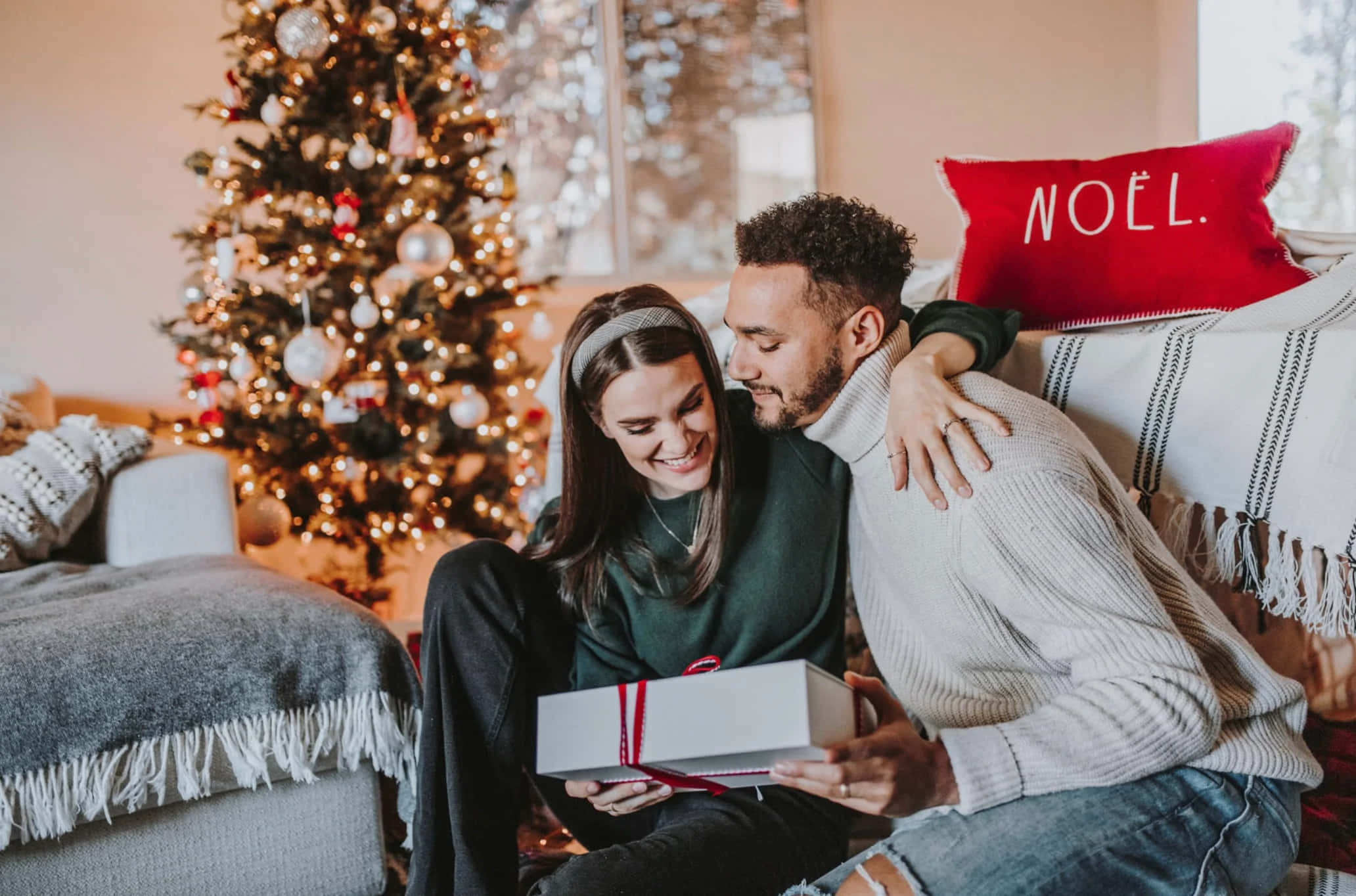 Couples Christmas 桌布 壁紙 — 一對微笑的情侶在閃爍的裝飾聖誕樹旁一起拆禮物，分享溫馨的聖誕時刻。