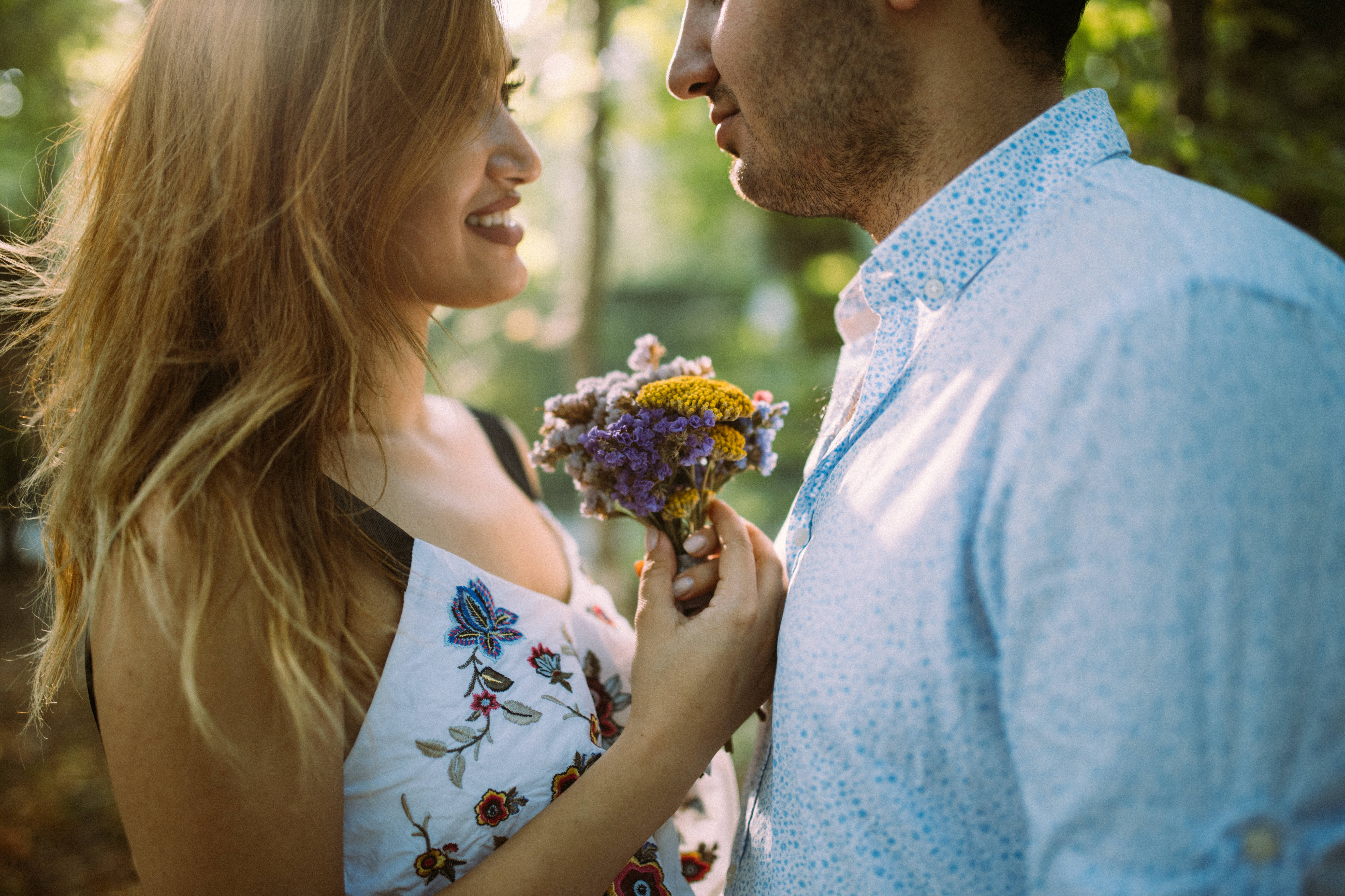 Romantic Love Flowers 桌布 壁紙 — 一對微笑的情侶在陽光明媚的森林中分享溫馨時刻，她向他獻上一束色彩繽紛的野花。