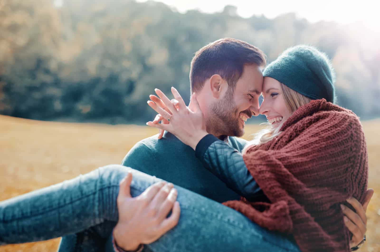 Cute Love 桌布 壁紙 — 一對微笑的情侶在陽光明媚的秋日田野中溫暖擁抱，身後是金色的草地和模糊的樹木。