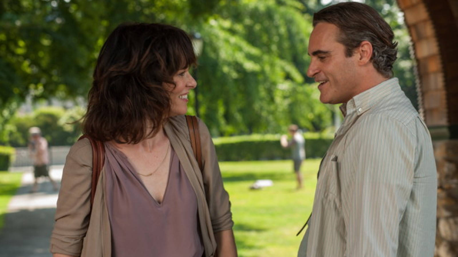 joaquin phoenix 桌布 壁紙 — 一對微笑的情侶在陽光普照的公園裡，在明亮的綠樹下進行溫暖的交談。