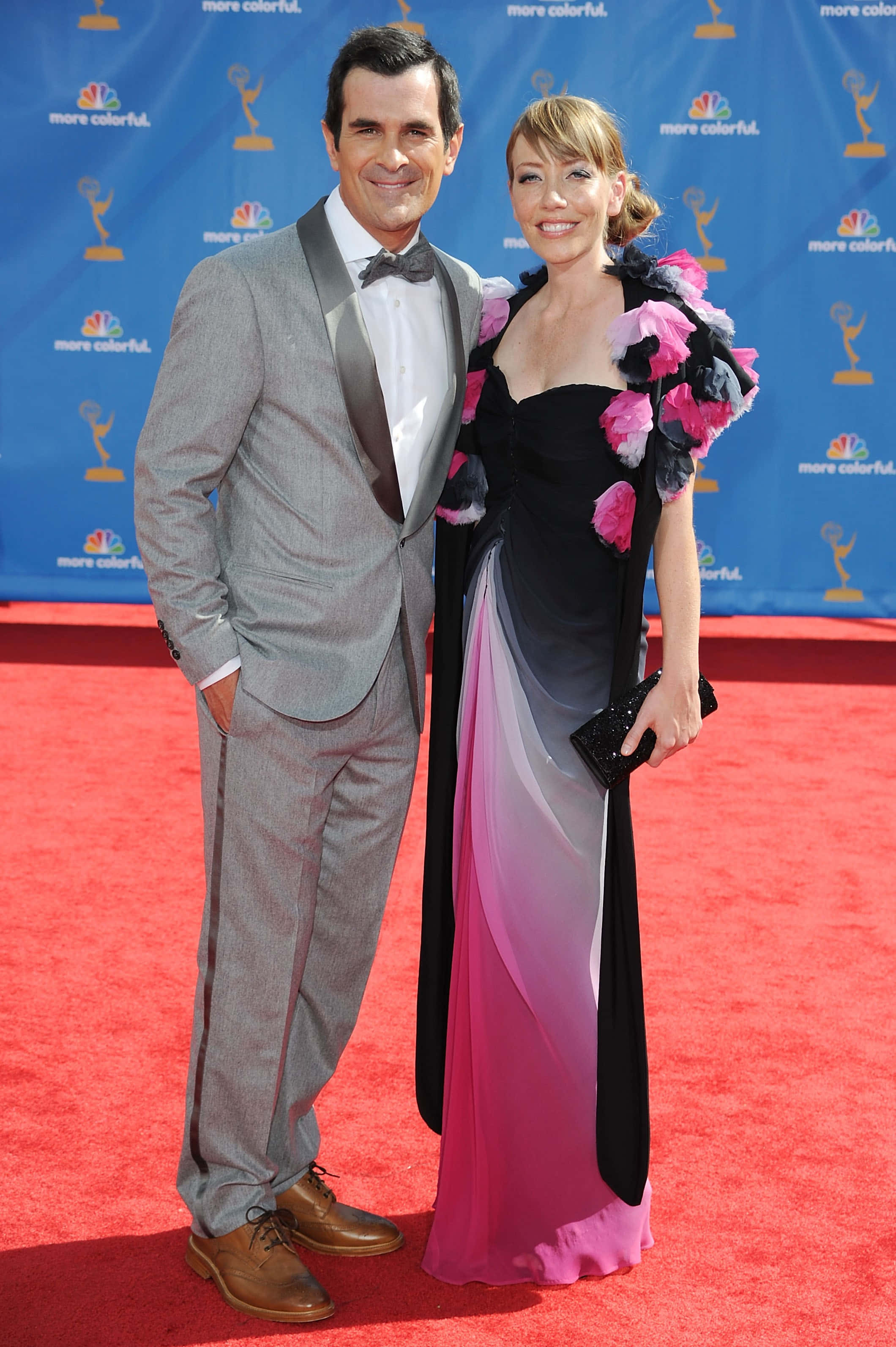 Ty Burrell 桌布 壁紙 — 一對微笑的情侶在頒獎典禮的紅地毯上擺姿勢，背景為藍色品牌背景。