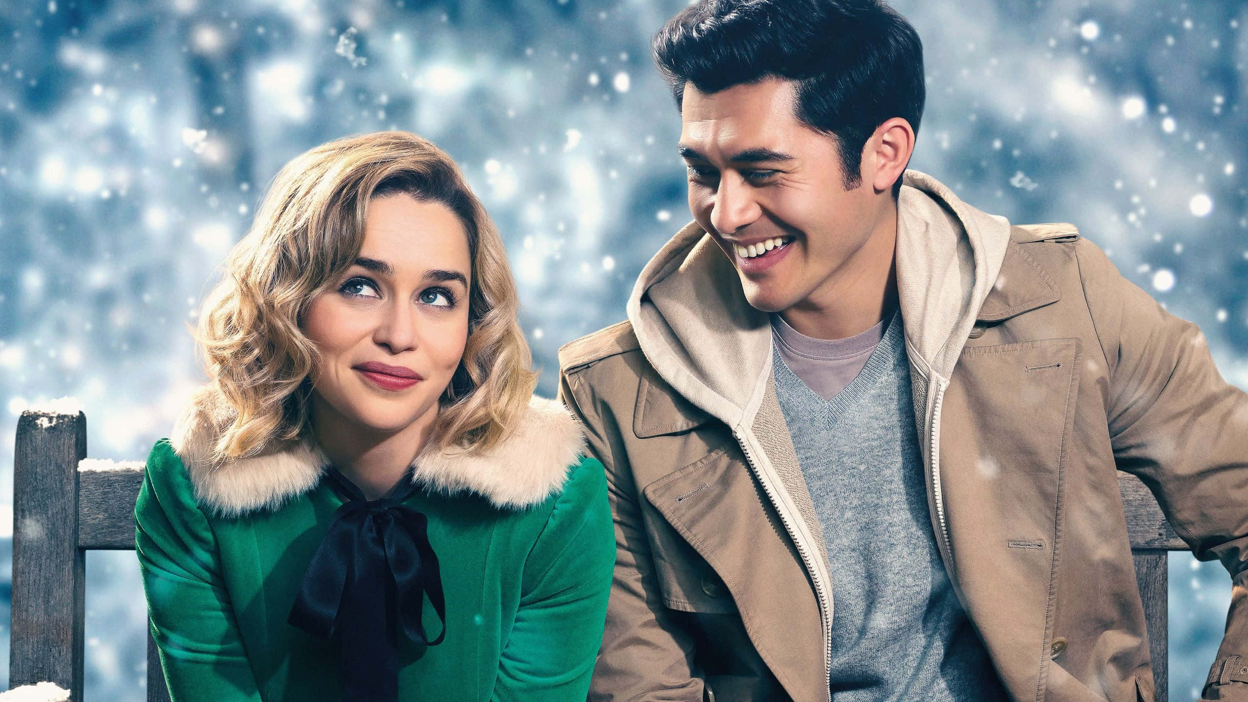 Christmas Movie 桌布 壁紙 — 一對微笑的情侶在飄雪中緊靠坐在積雪的長椅上，背景是冬日藍天。