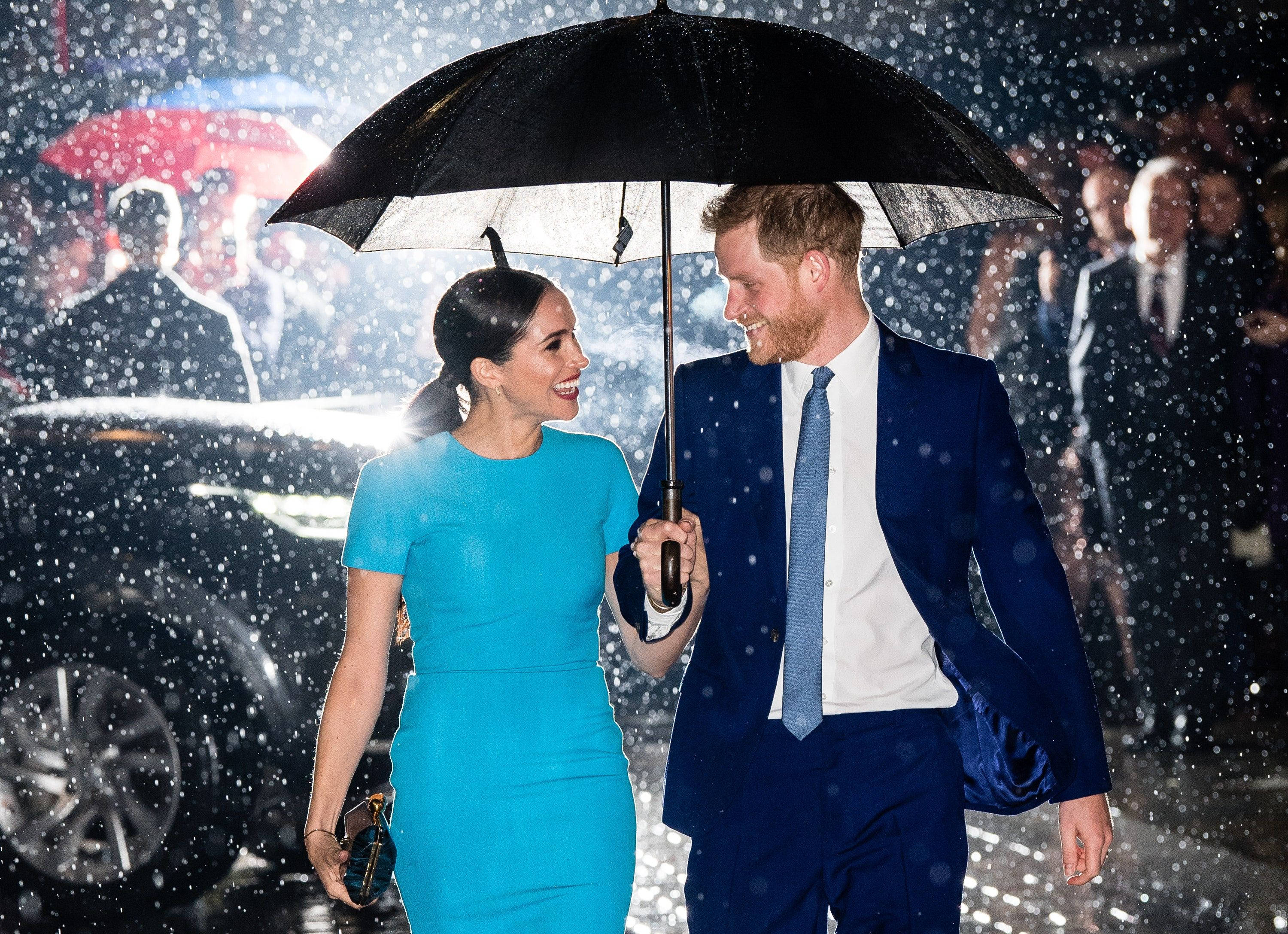 Meghan Markle 桌布 壁紙 — 一對微笑的情侶在黑色雨傘下於大雨中行走，身後濕漉漉的人行道上反射著城市燈光。
