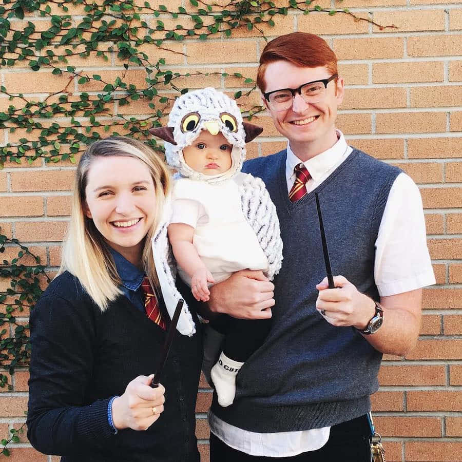 Family 桌布 壁紙 — 一對微笑的情侶穿著哈利波特服裝，與他們打扮成貓頭鷹的寶寶在佈滿常春藤的磚牆前擺姿勢。