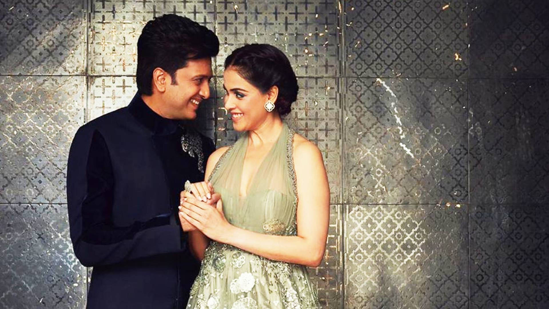riteish deshmukh 桌布 壁紙 — 一對微笑的情侶穿著正式服裝，在圖案金屬牆前牽手，呈現華麗肖像。