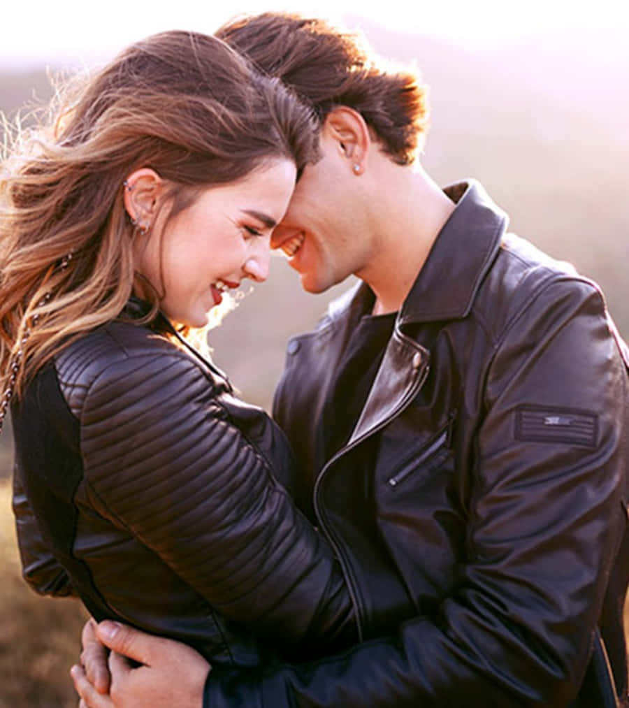 Romantic Love 桌布 壁紙 — 一對微笑的情侶穿著黑色皮夾克，在戶外金色陽光照亮他們的臉龐時溫柔地擁抱。