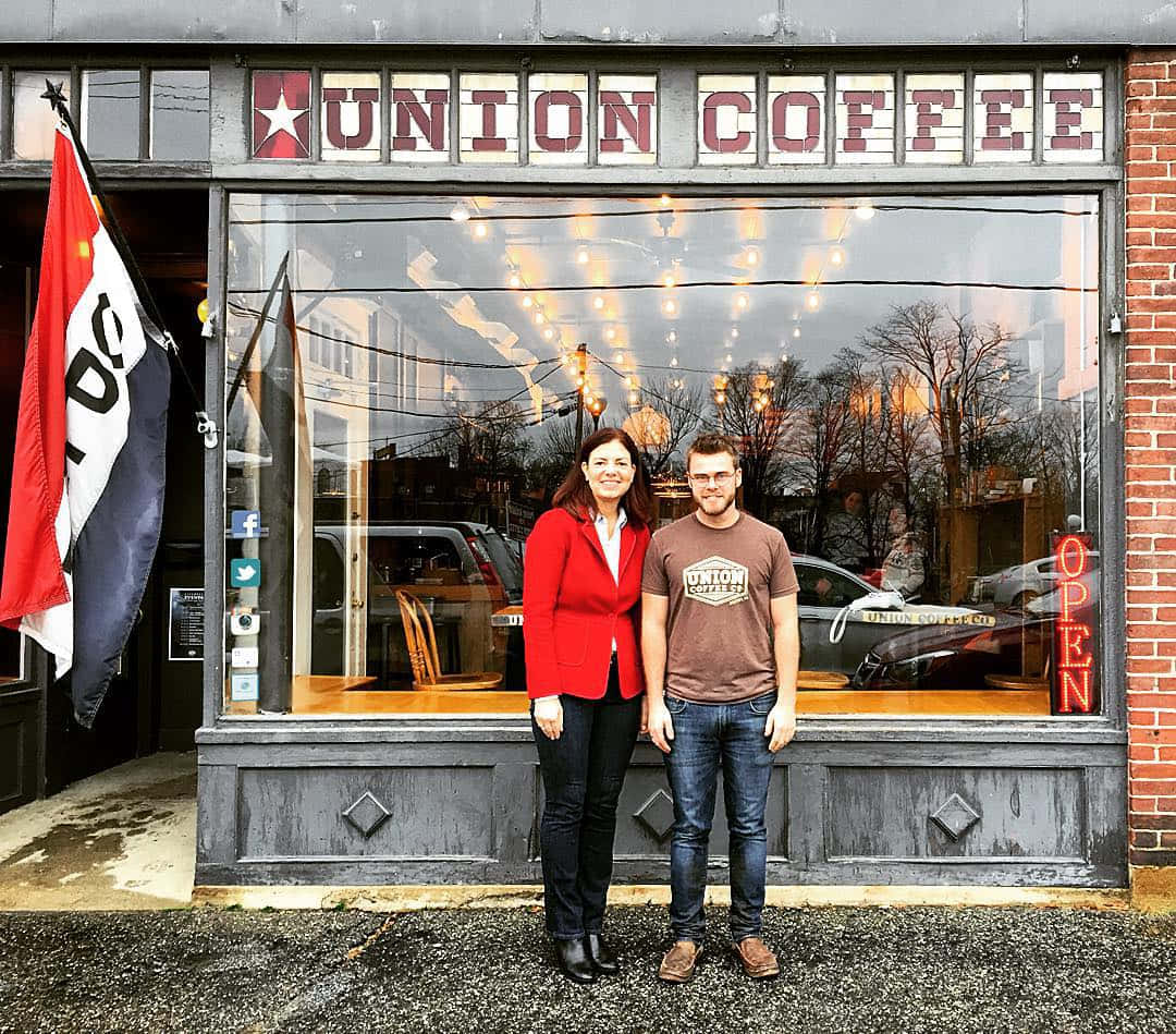 government 桌布 壁紙 — 一對微笑的情侶站在Union Coffee店外，磚砌外牆和窗內閃爍的串燈。