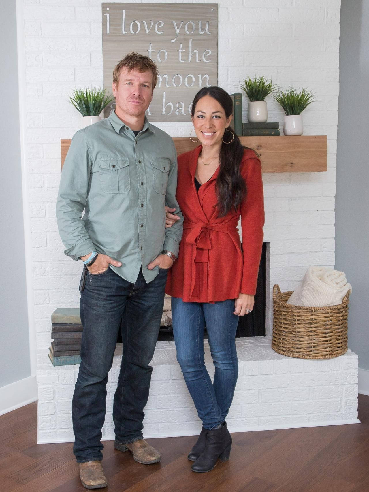 Joanna 桌布 壁紙 — 一對微笑的情侶站在白色磚砌壁爐前，壁爐上有木製壁爐架和盆栽植物。