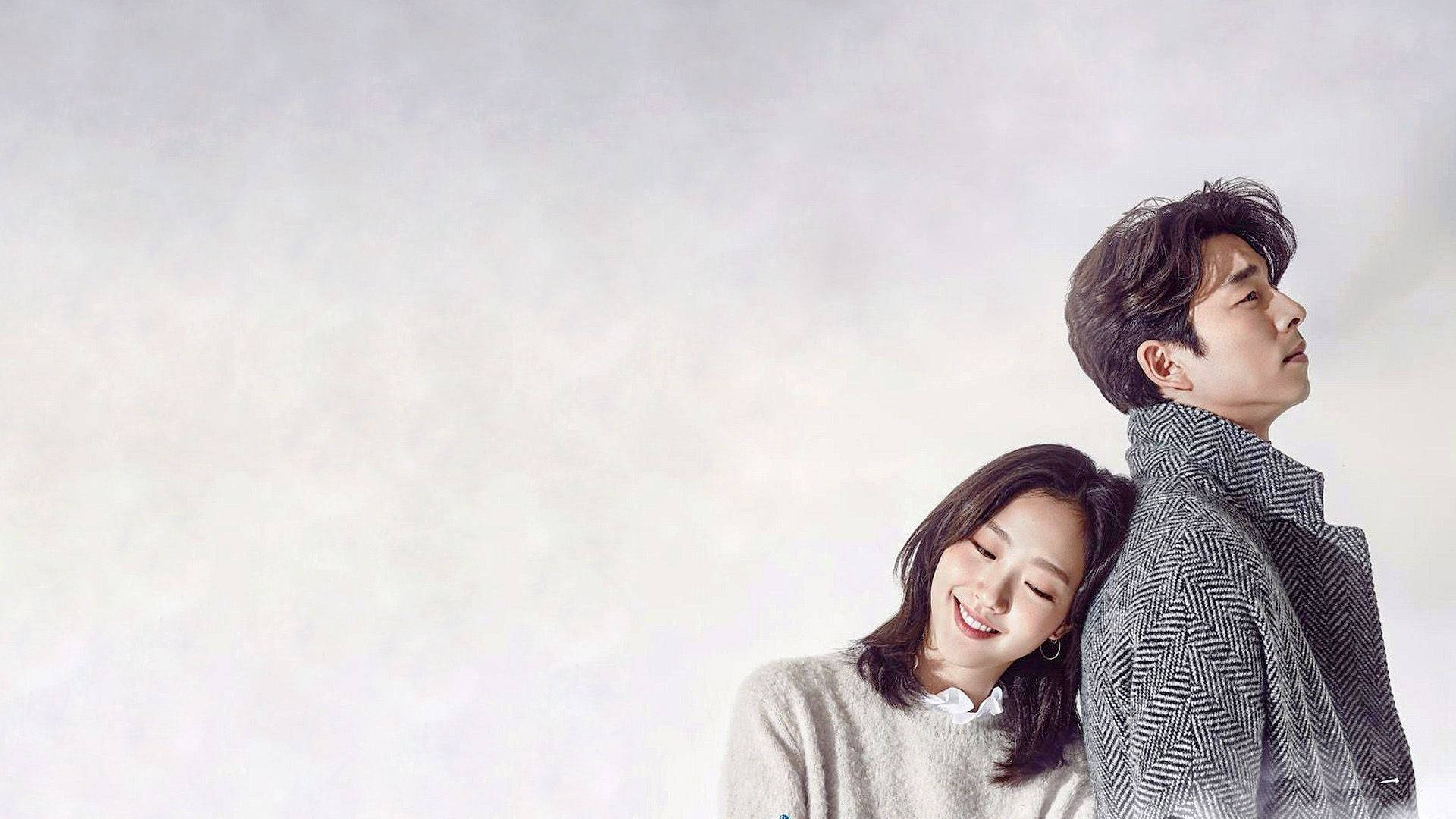 kdrama 桌布 壁紙 — 一對微笑的情侶背靠背靠在一面柔軟有紋理的灰色牆上，姿勢溫柔而親密。