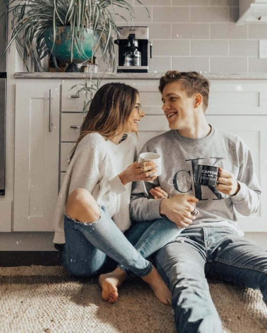 Cute Boyfriend 桌布 壁紙 — 一對微笑的情侶赤腳坐在明亮廚房地毯上，手持咖啡杯，互相凝視。