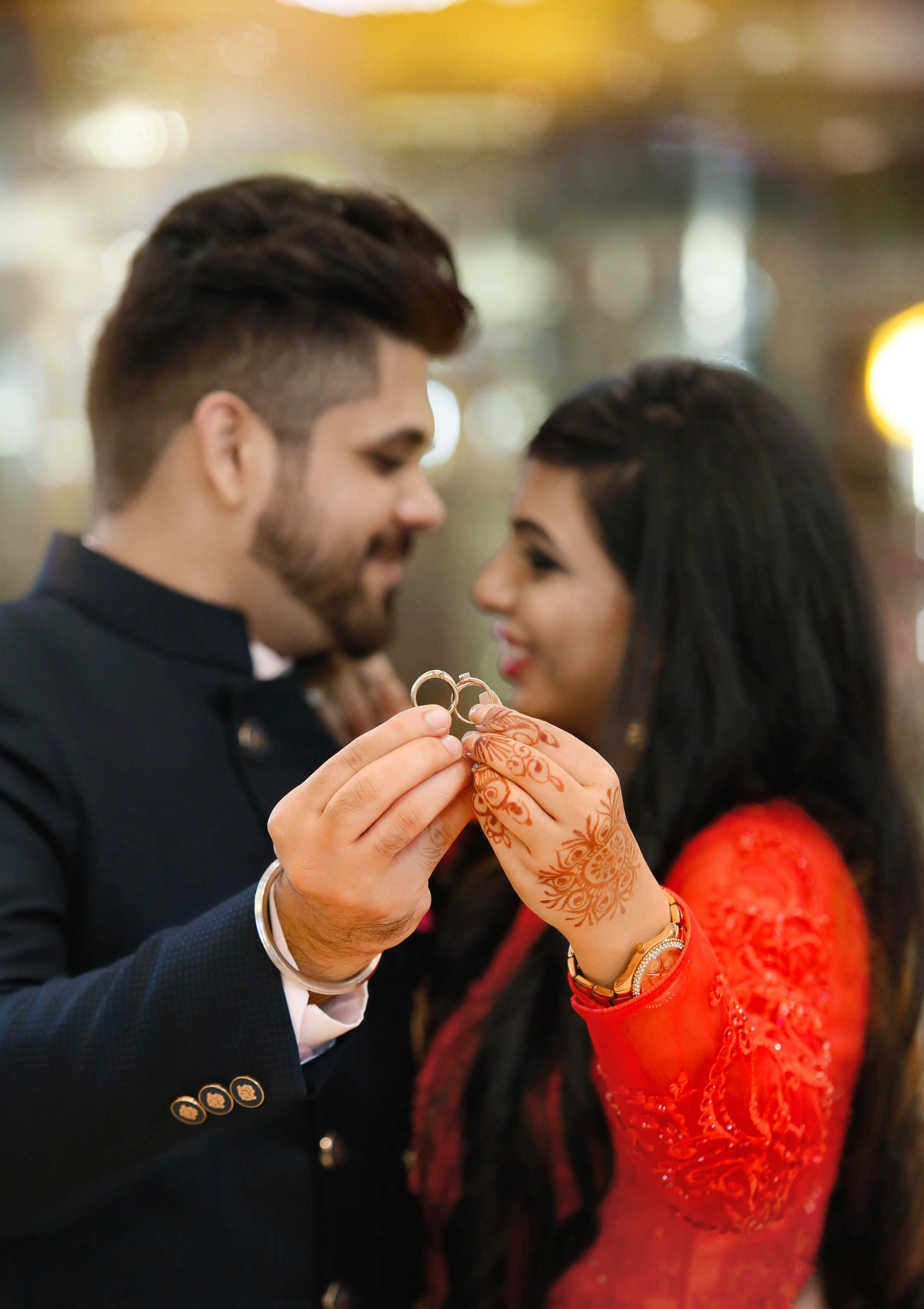 Indian 桌布 壁紙 — 一對微笑的新人交換結婚戒指，她手上帶有精緻的指甲花圖案，背景是溫暖的模糊光線。