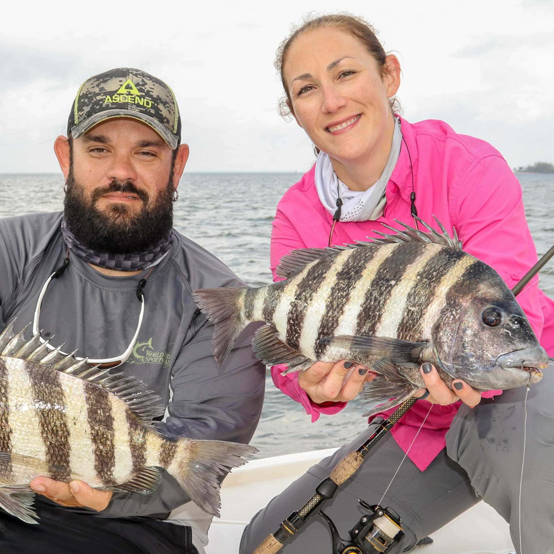 Sheepshead Fish 桌布 壁紙 — 一對微笑的男女在船上自豪地展示他們捕獲的大型條紋魚，背景是平靜的海洋。