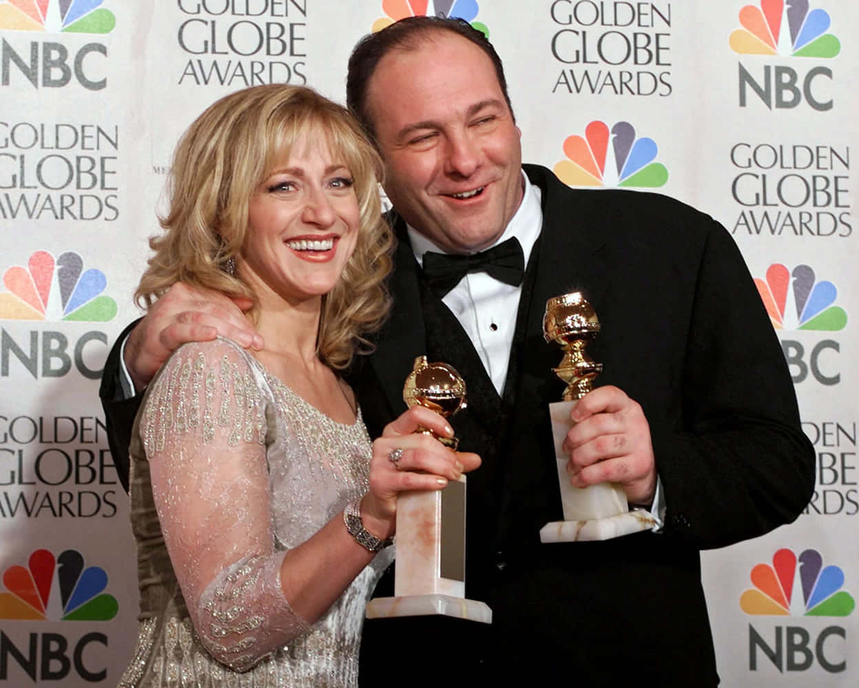 James Gandolfini 桌布 壁紙 — 一對微笑的男女穿著正式服裝，在品牌活動背景前一起拿著金球獎獎盃擺姿勢。