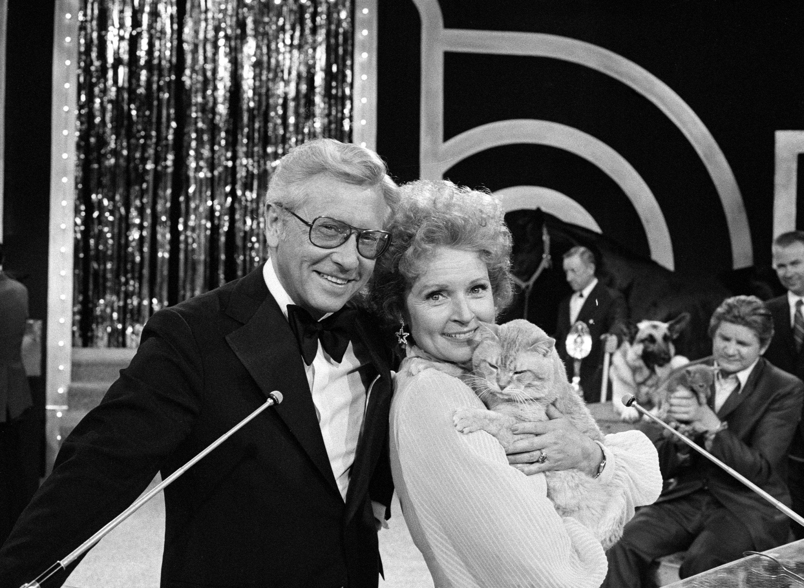 Betty White 桌布 壁紙 — 一對微笑的老年夫婦穿著正裝，在閃閃發光的舞台上擺姿勢，女人抱著一隻貓。