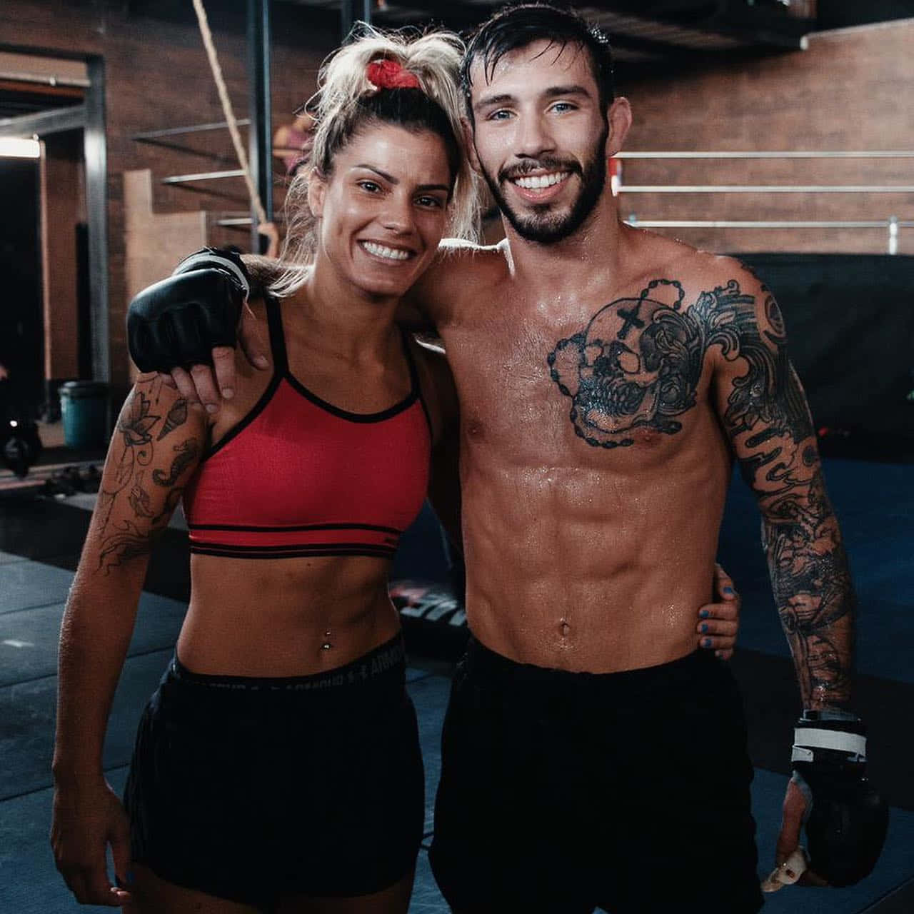 MMA 桌布 壁紙 — 一對微笑的肌肉情侶帶有刺青，在健身房一起擺姿勢，戴著拳擊手套和運動服。