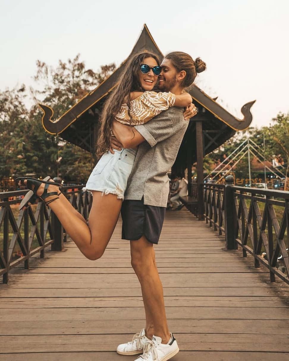 Boyfriend And Girlfriend 桌布 壁紙 — 一對快樂的情侶在傳統泰式亭閣下的木橋上擁抱，背景是茂密的綠植。
