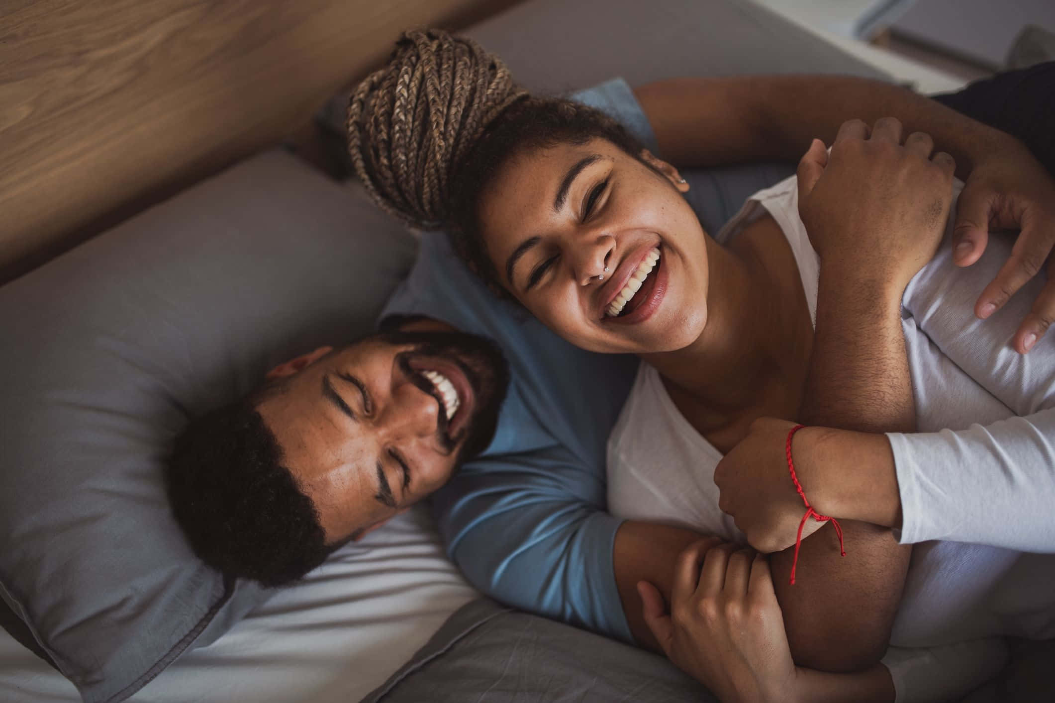 Cuddle 桌布 壁紙 — 一對快樂的情侶在床上一起大笑，在柔和自然光下溫暖地擁抱。