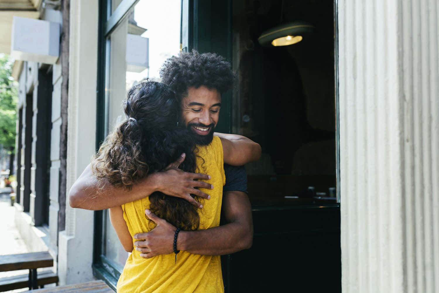 Hug 桌布 壁紙 — 一對快樂的情侶在店鋪門前溫暖擁抱，陽光穿過玻璃門灑落。