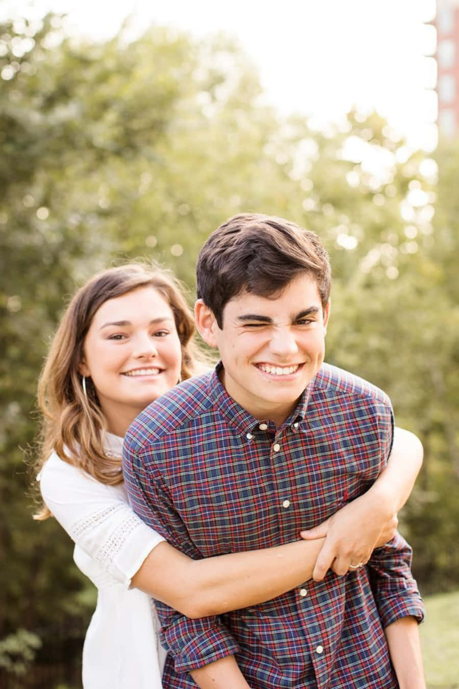 Brother And Sister 桌布 壁紙 — 一對快樂的情侶在戶外擁抱，溫暖的陽光透過他們身後綠樹的縫隙灑落。
