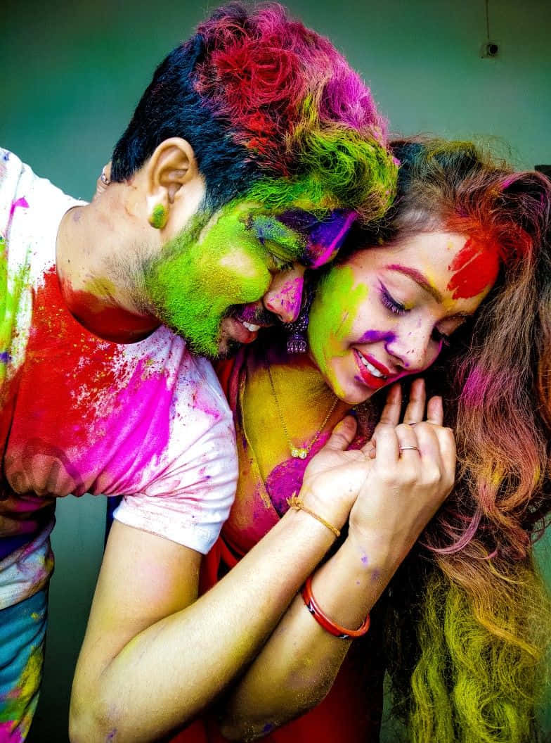 Holi 桌布 壁紙 — 一對快樂的情侶在純綠色牆壁前擁抱，身上佈滿鮮豔的彩色粉末。