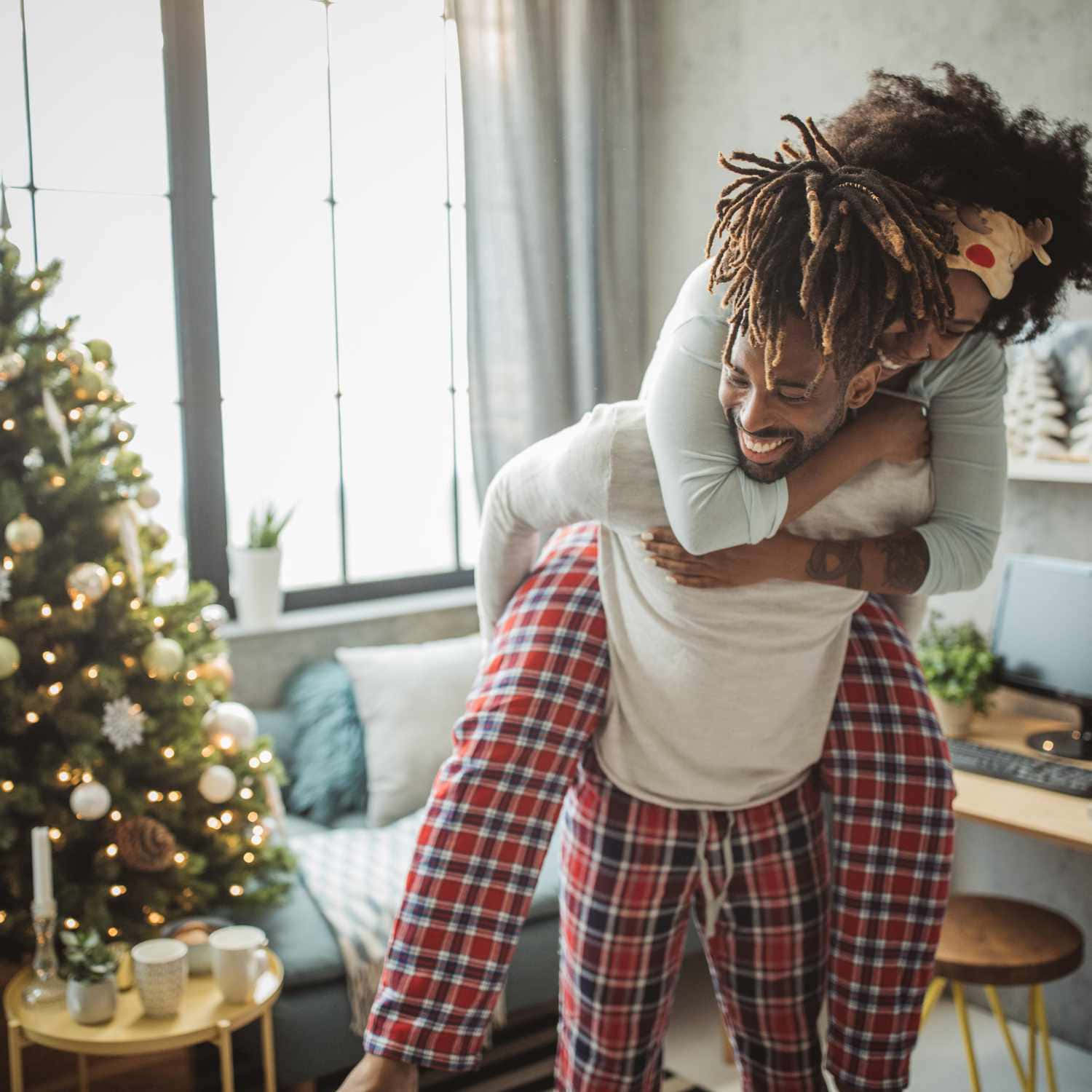 Couples Christmas 桌布 壁紙 — 一對快樂的情侶穿著睡衣，在舒適的客廳裡，旁邊是裝飾好的聖誕樹，玩著俏皮的背人遊戲。
