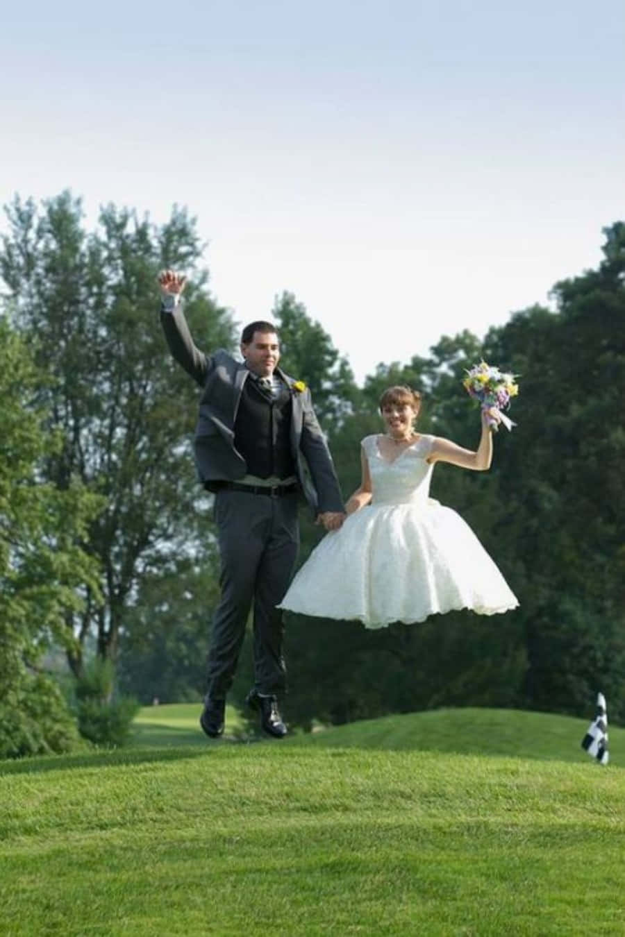 Funny Wedding 桌布 壁紙 — 一對快樂的新人在陽光明媚的高爾夫球場上跳躍，身後是茂密的綠樹。