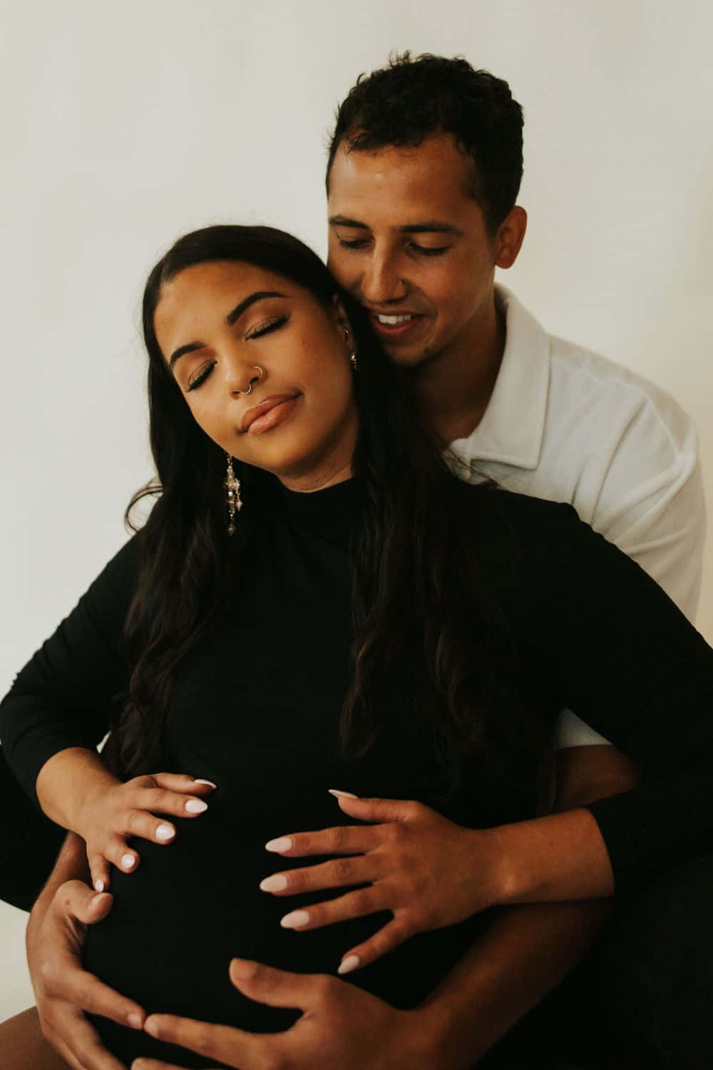 Pregnant 桌布 壁紙 — 一對恩愛的情侶溫柔地擁抱，男人輕輕地捧著孕婦的肚子，背景是柔和的白色。