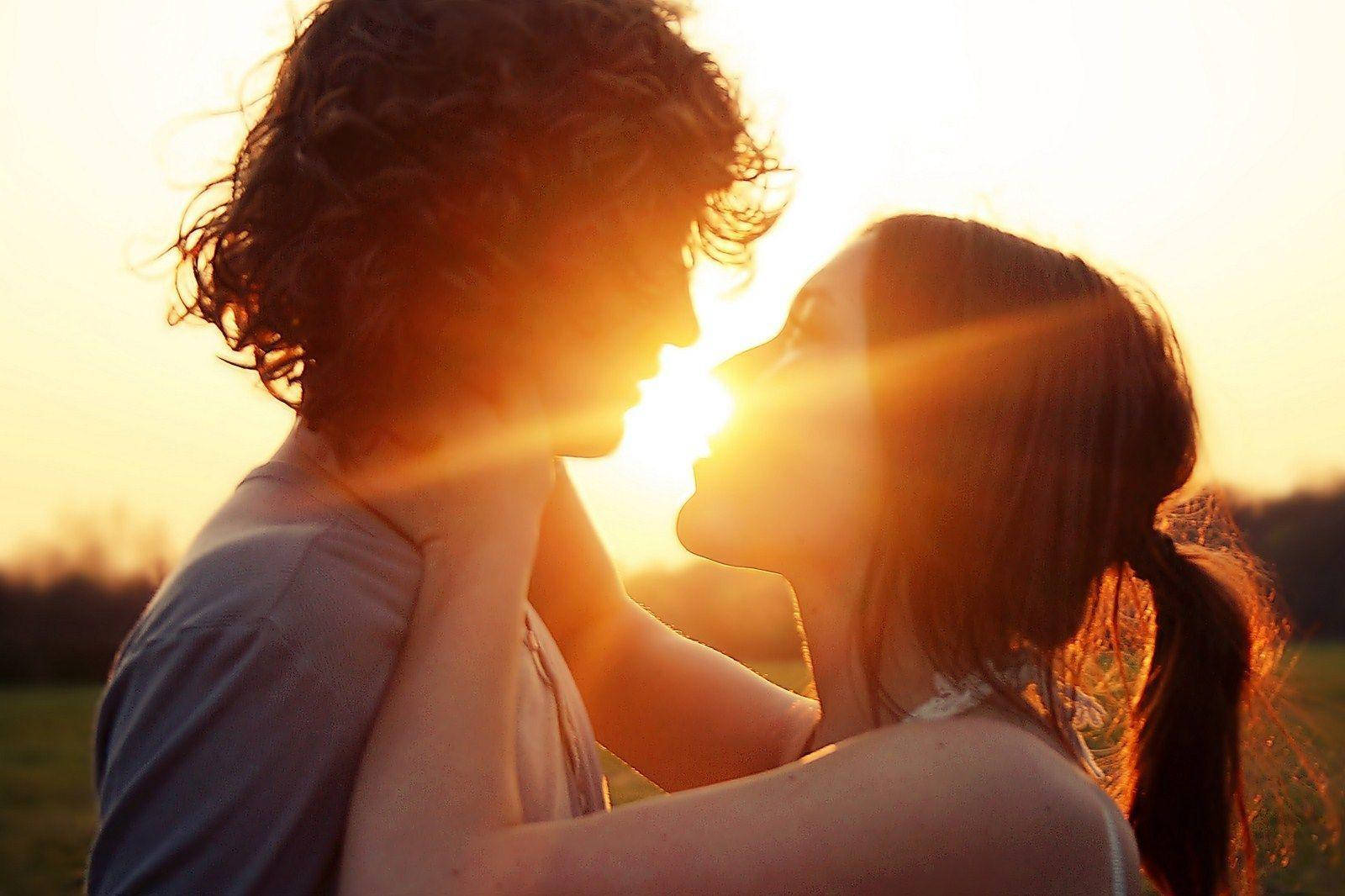 Romantic Couples 桌布 壁紙 — 一對情侶以剪影分享親密時刻，金色夕陽的光芒在他們臉龐之間閃爍，背景是草地。