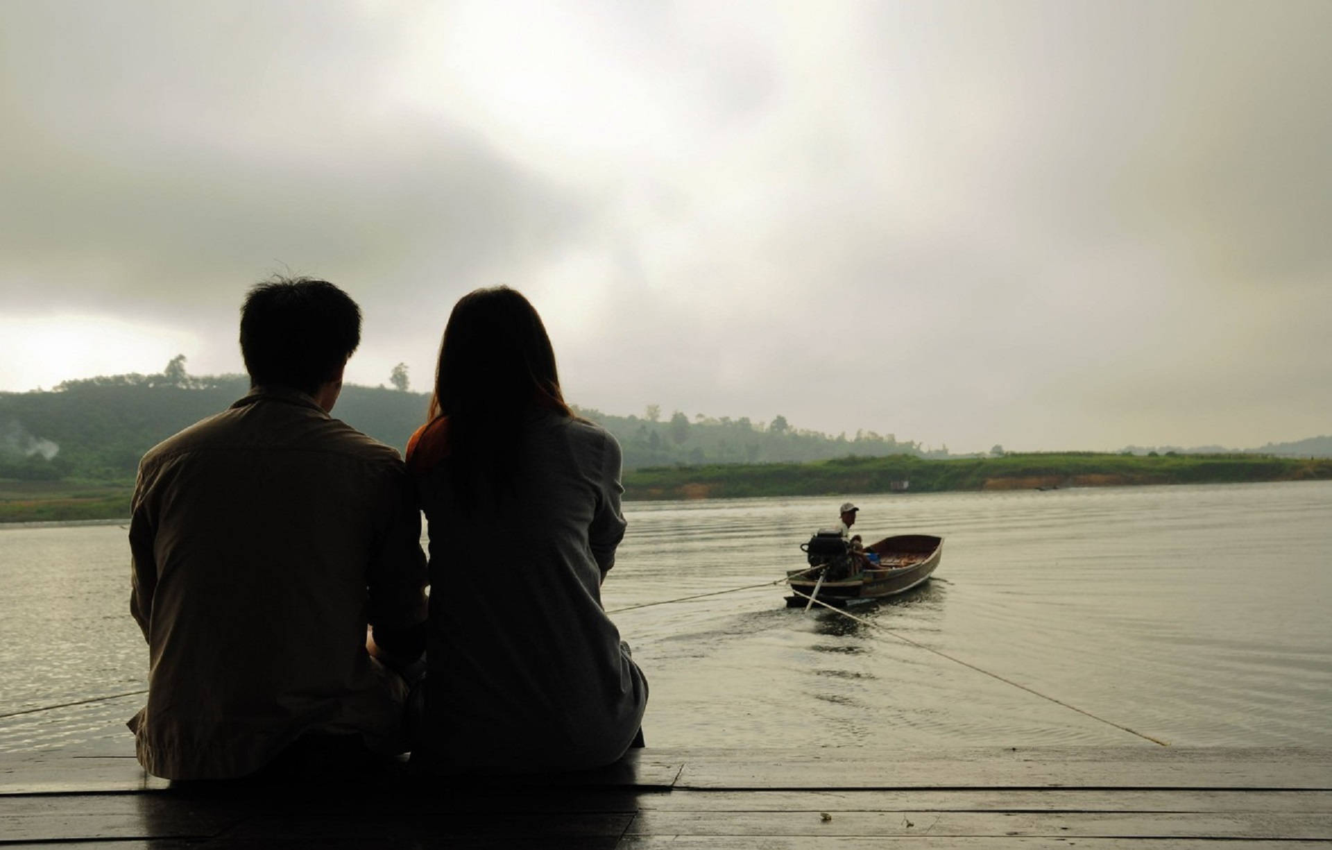 Romantic Love 桌布 壁紙 — 一對情侶以剪影形式坐在木碼頭上，觀看霧氣瀰漫的河上一艘小船中的孤獨漁夫，天空多雲。