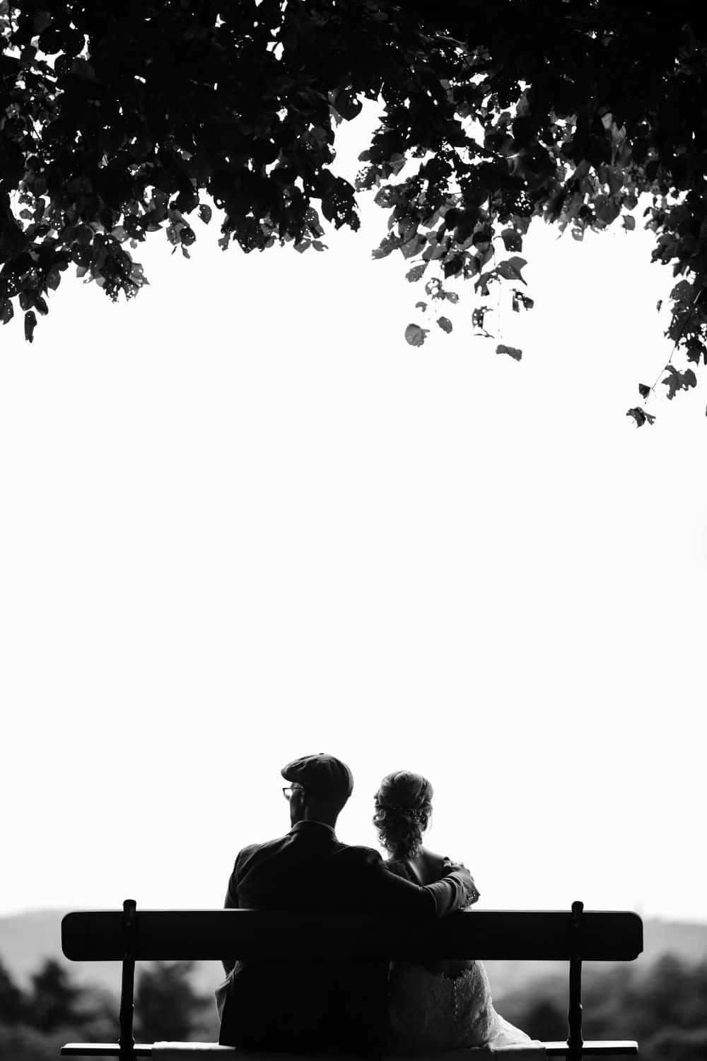 Lovers 桌布 壁紙 — 一對情侶以剪影形式坐在長椅上，上方是枝葉茂密的樹枝，背景是明亮的天空。