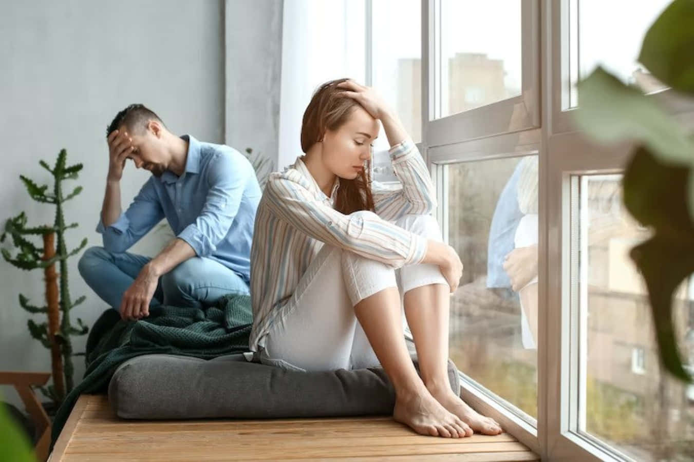 Breakup Couple 桌布 壁紙 — 一對情侶分開坐在現代公寓的窗台上，兩人都顯得悲傷和壓力，一隻手放在頭上。