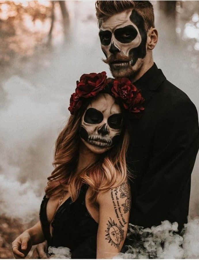 Creepy Halloween 桌布 壁紙 — 一對情侶化著骷髏妝容、手持紅玫瑰，在煙霧瀰漫的森林中於黃金時刻擁抱。