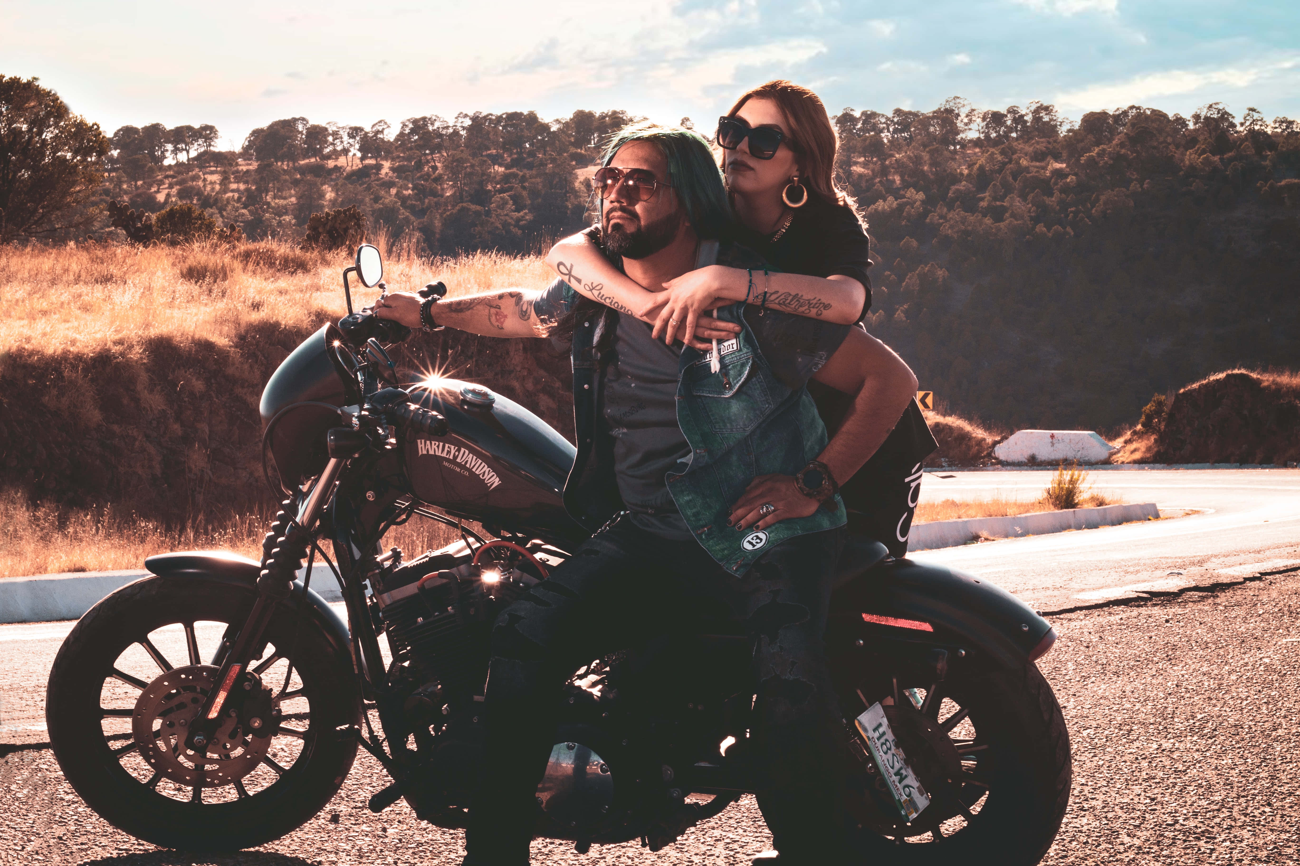 愛心 桌布 壁紙 — 一對情侶在停泊在陽光明媚路邊的Harley-Davidson機車上擁抱，背景是金色的山丘和樹木。